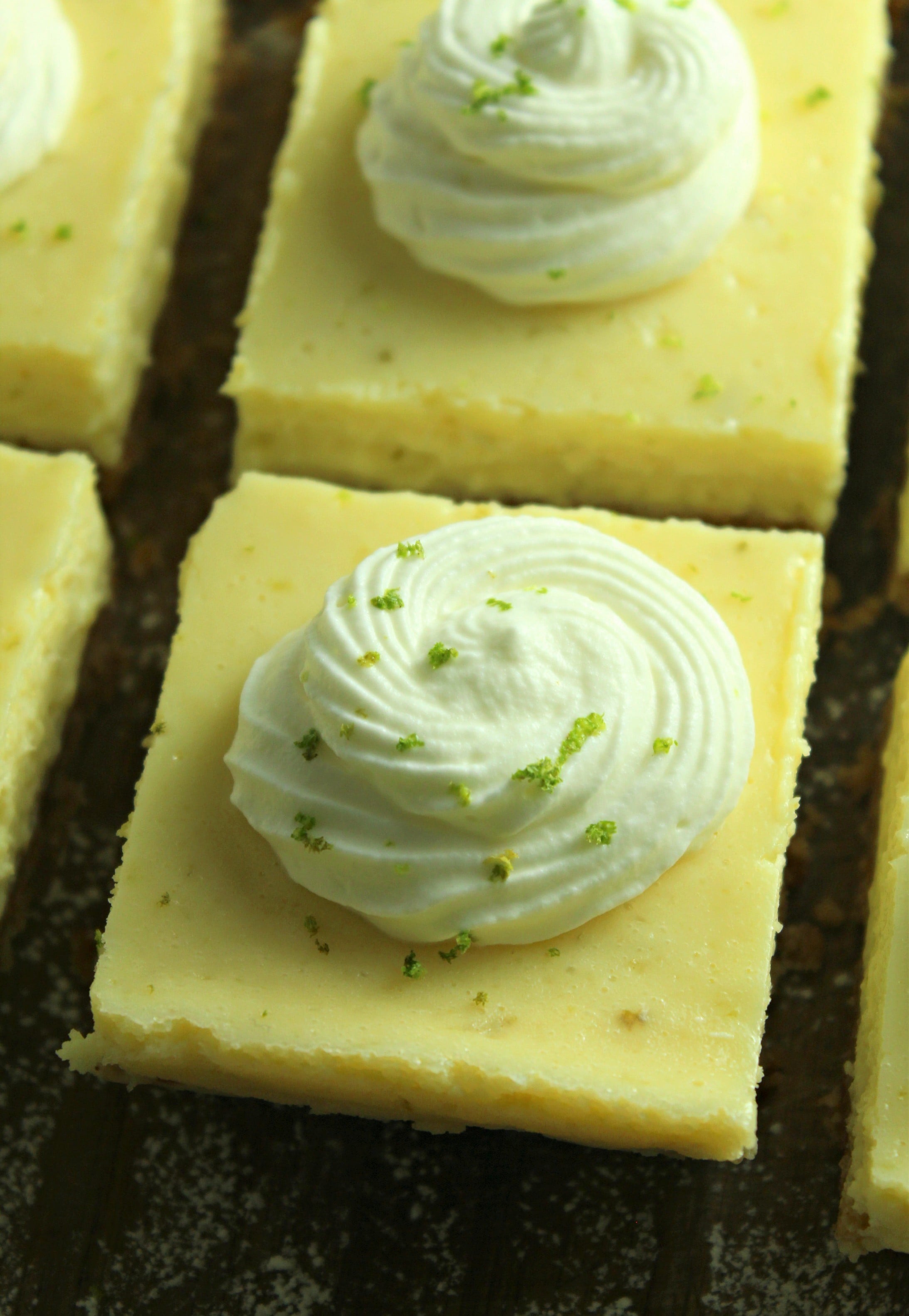 Key Lime Bars with lime whipped cream topped with lime zest on a baking sheet