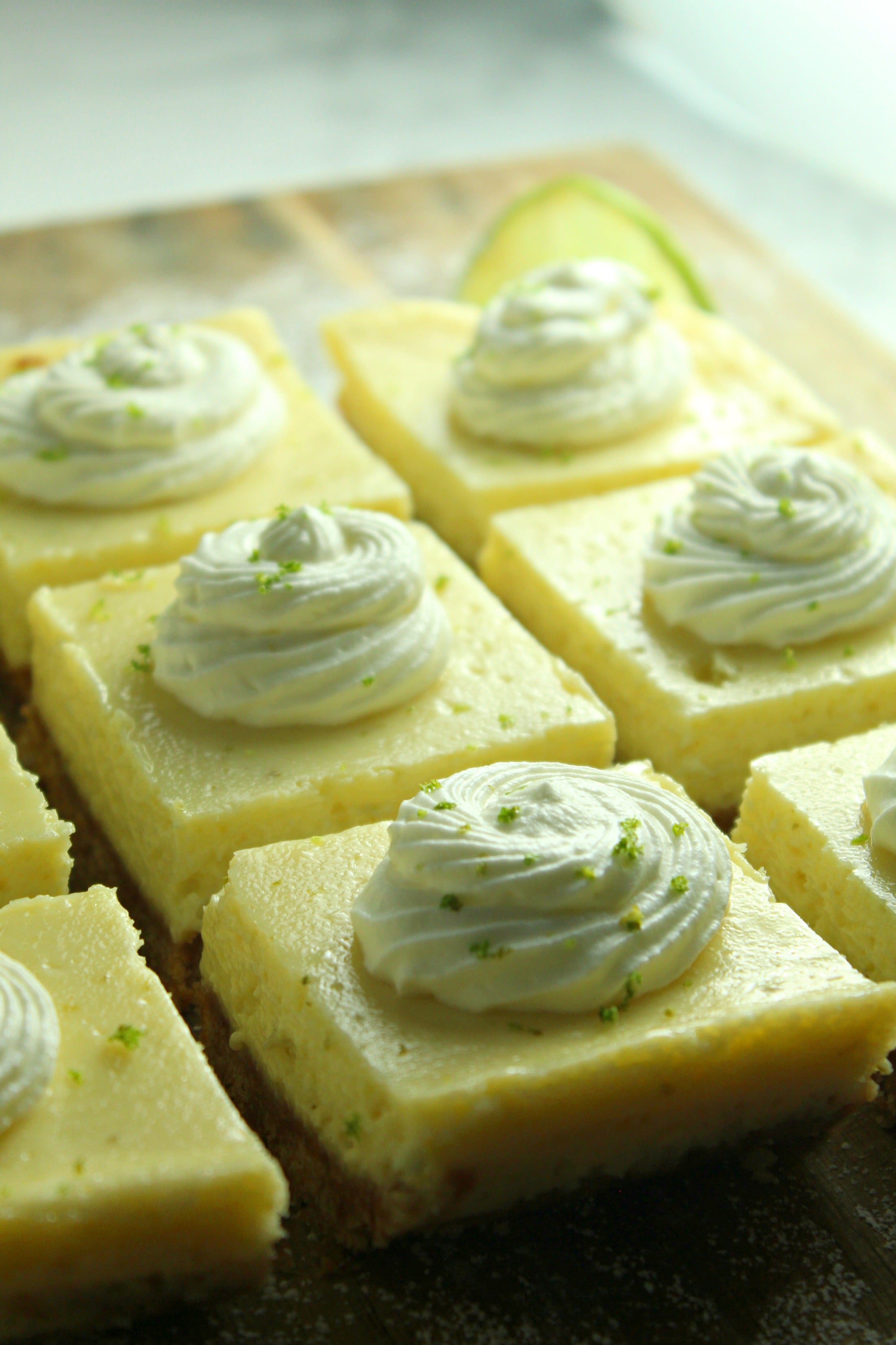 Key Lime Bars with lime whipped cream topped with lime zest on a baking sheet from the side