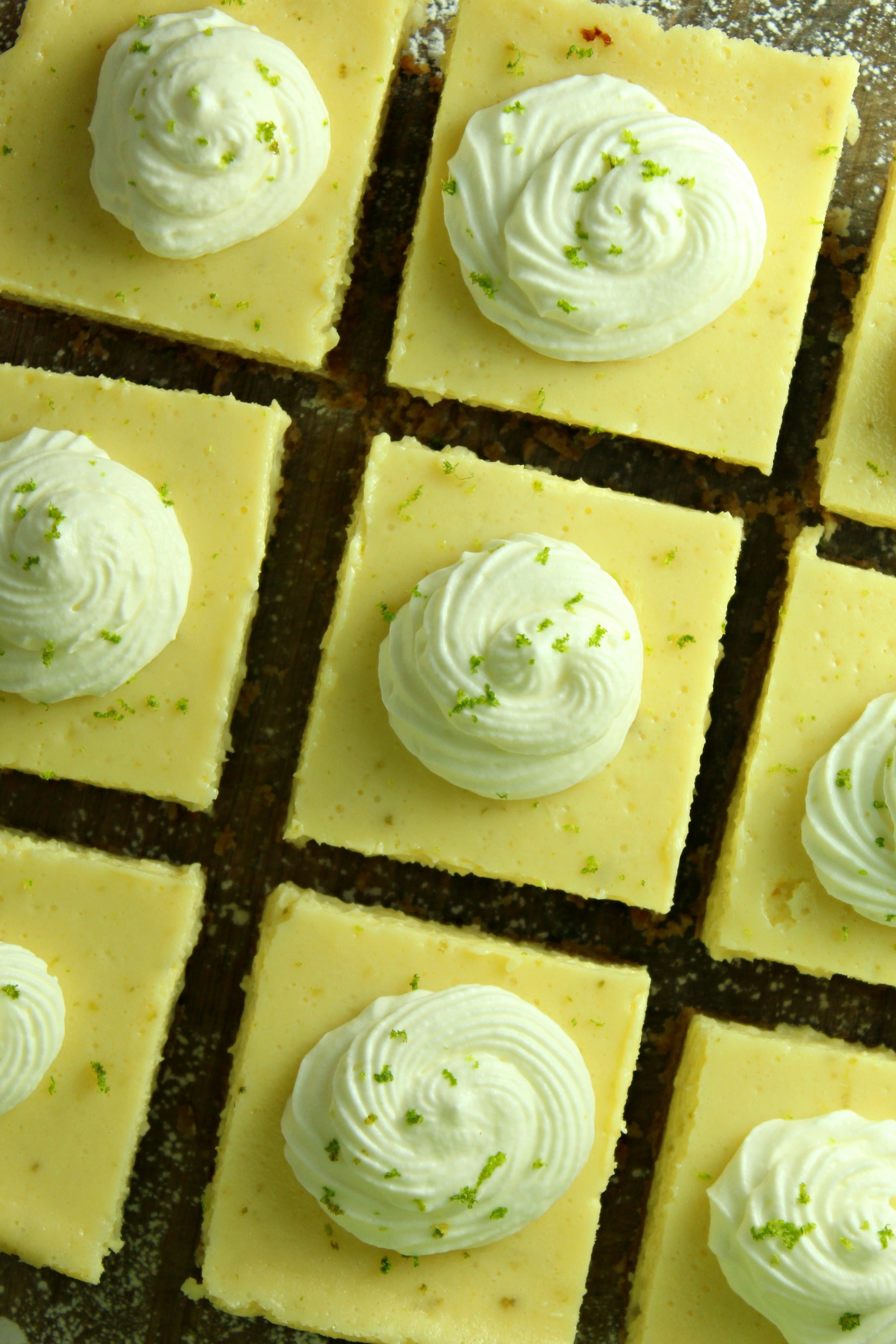 Key Lime Bars with lime whipped cream topped with lime zest on a baking sheet overhead