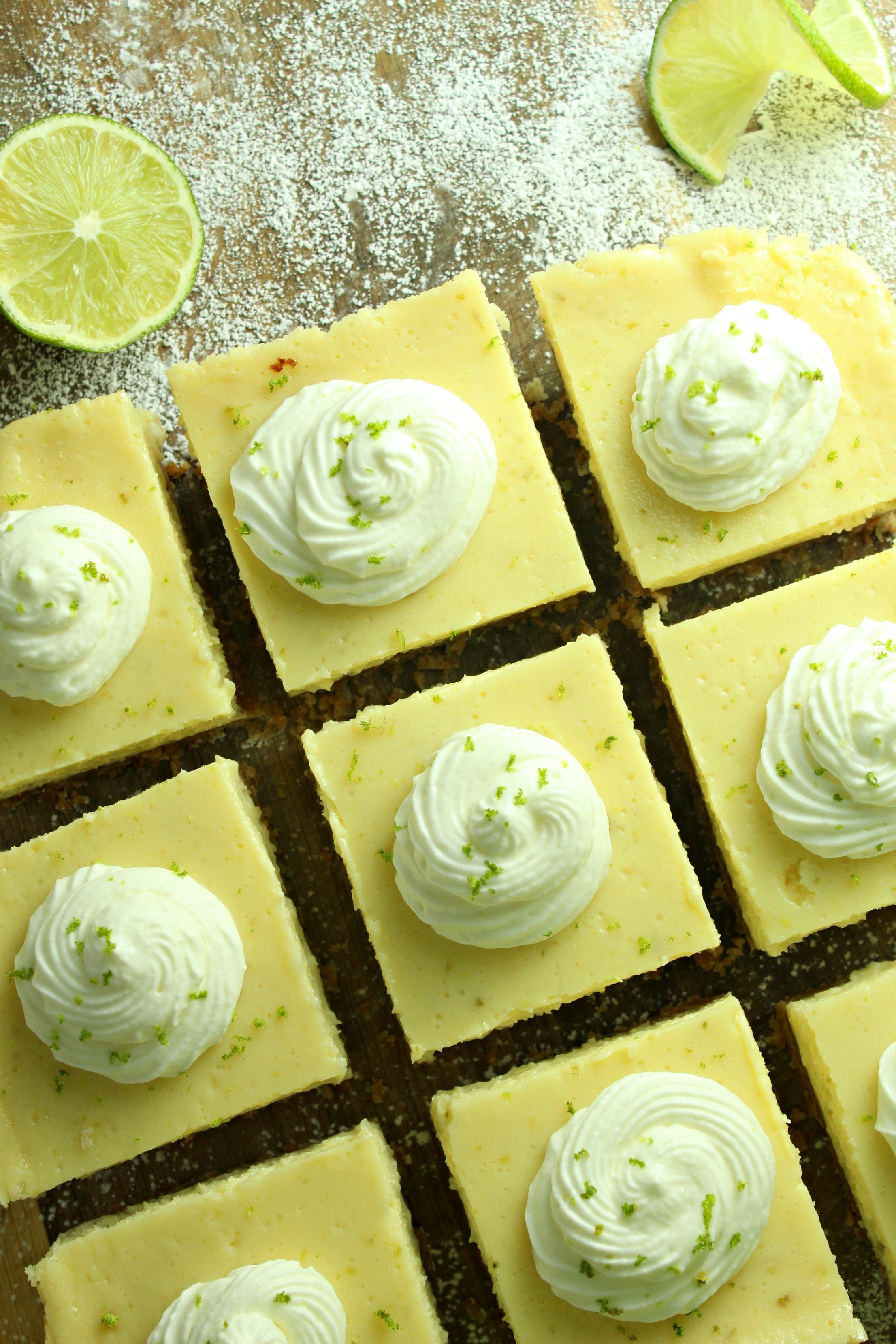 Key Lime Bars with lime whipped cream topped with lime zest on a baking sheet