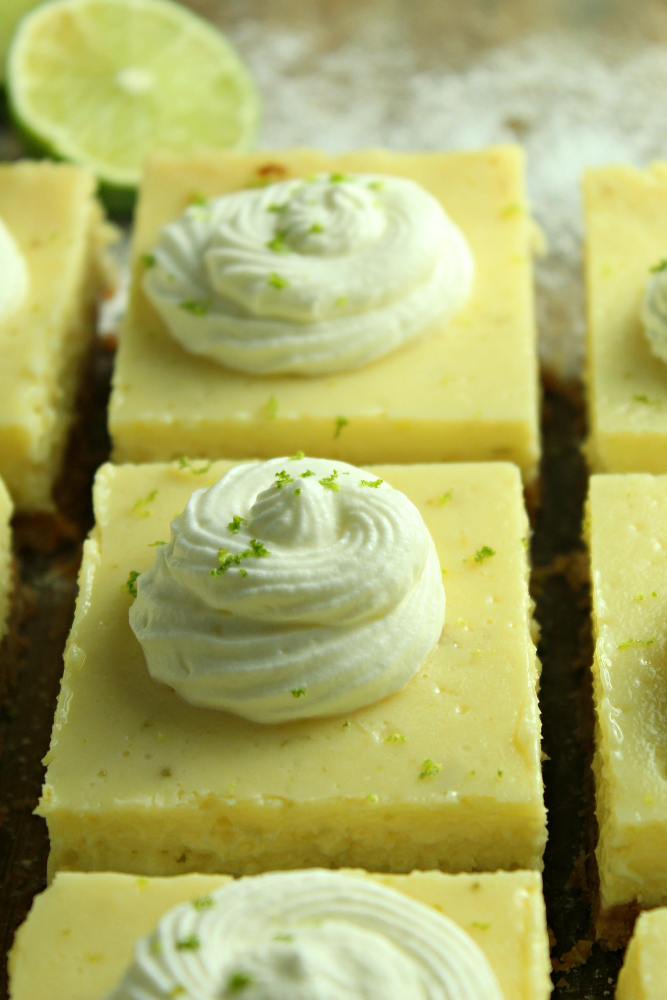Key Lime Bars with lime whipped cream topped with lime zest on a baking sheet
