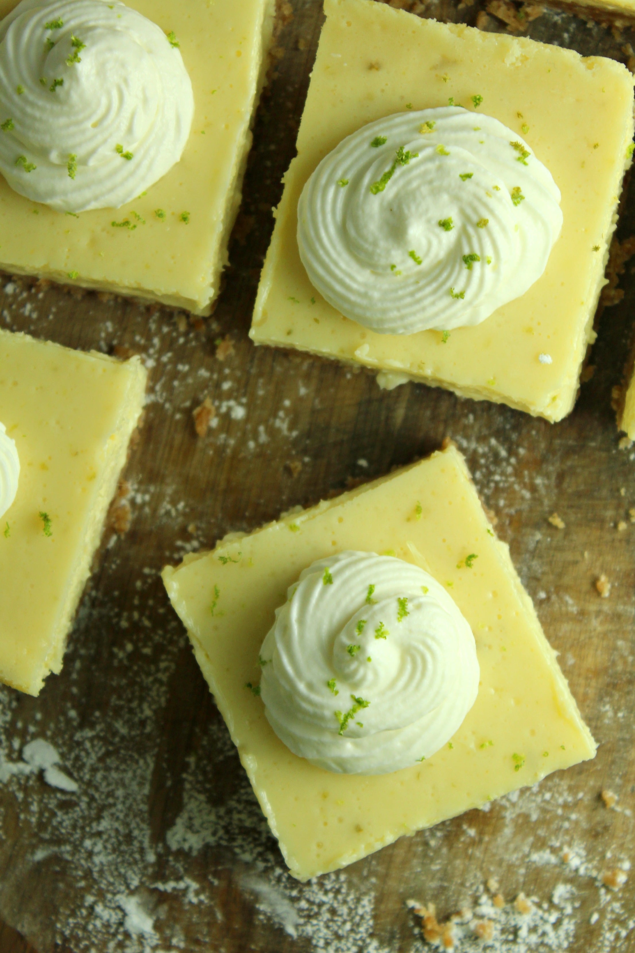 Key Lime Bars with lime whipped cream topped with lime zest on a wood table