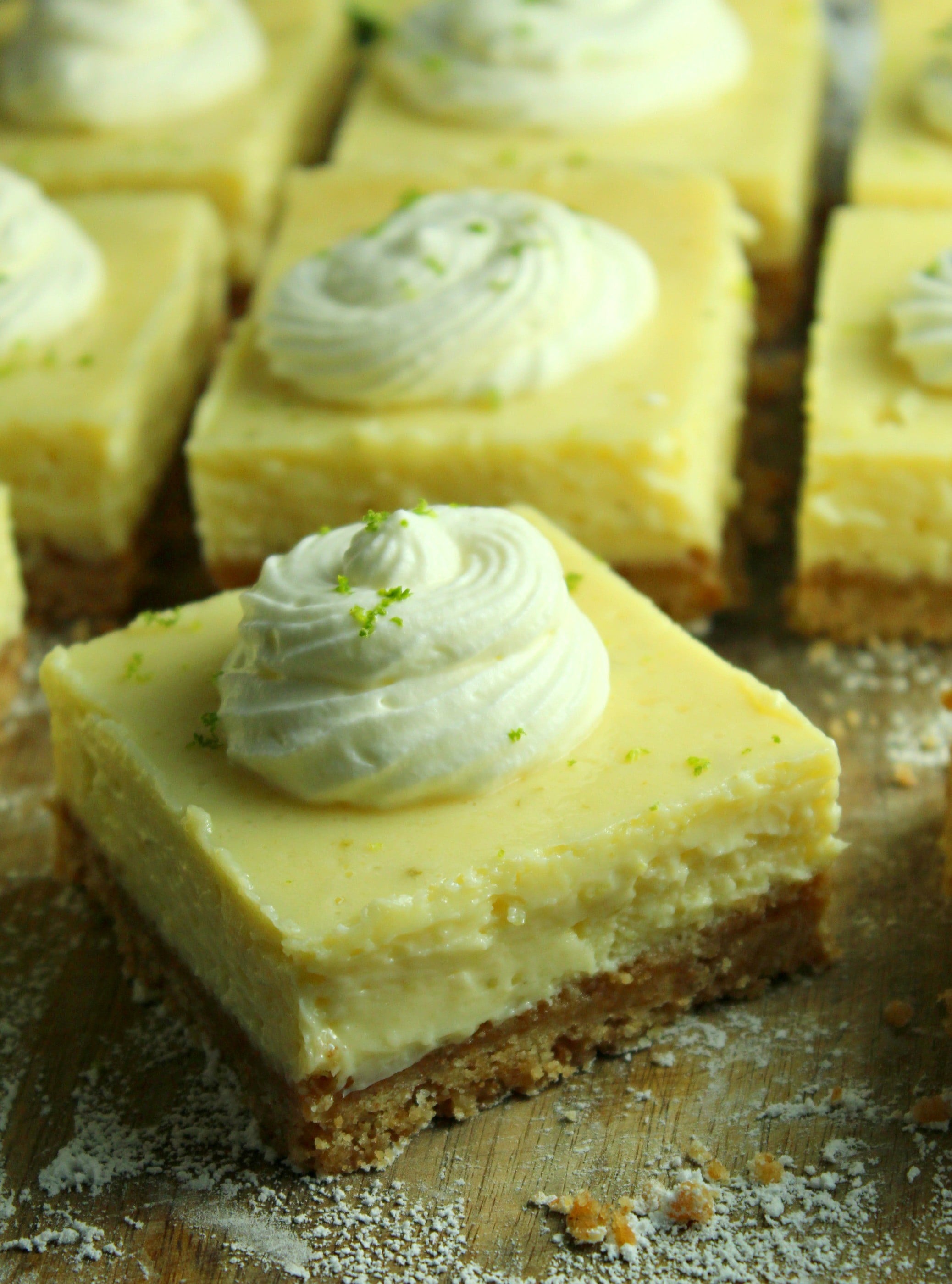 Key Lime Bars with lime whipped cream topped with lime zest on a table