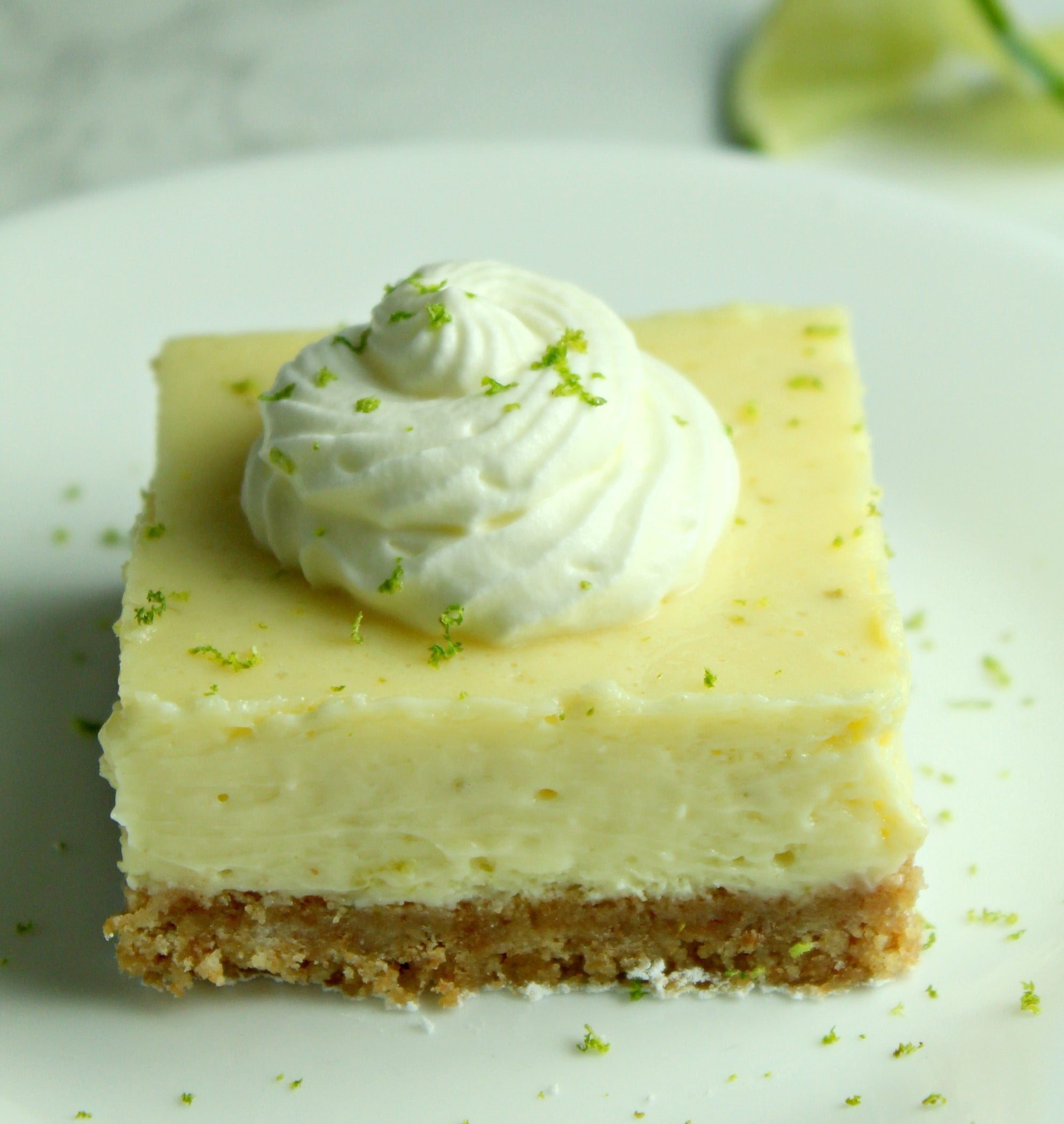Key Lime Bars with lime whipped cream topped with lime zest on a white plate