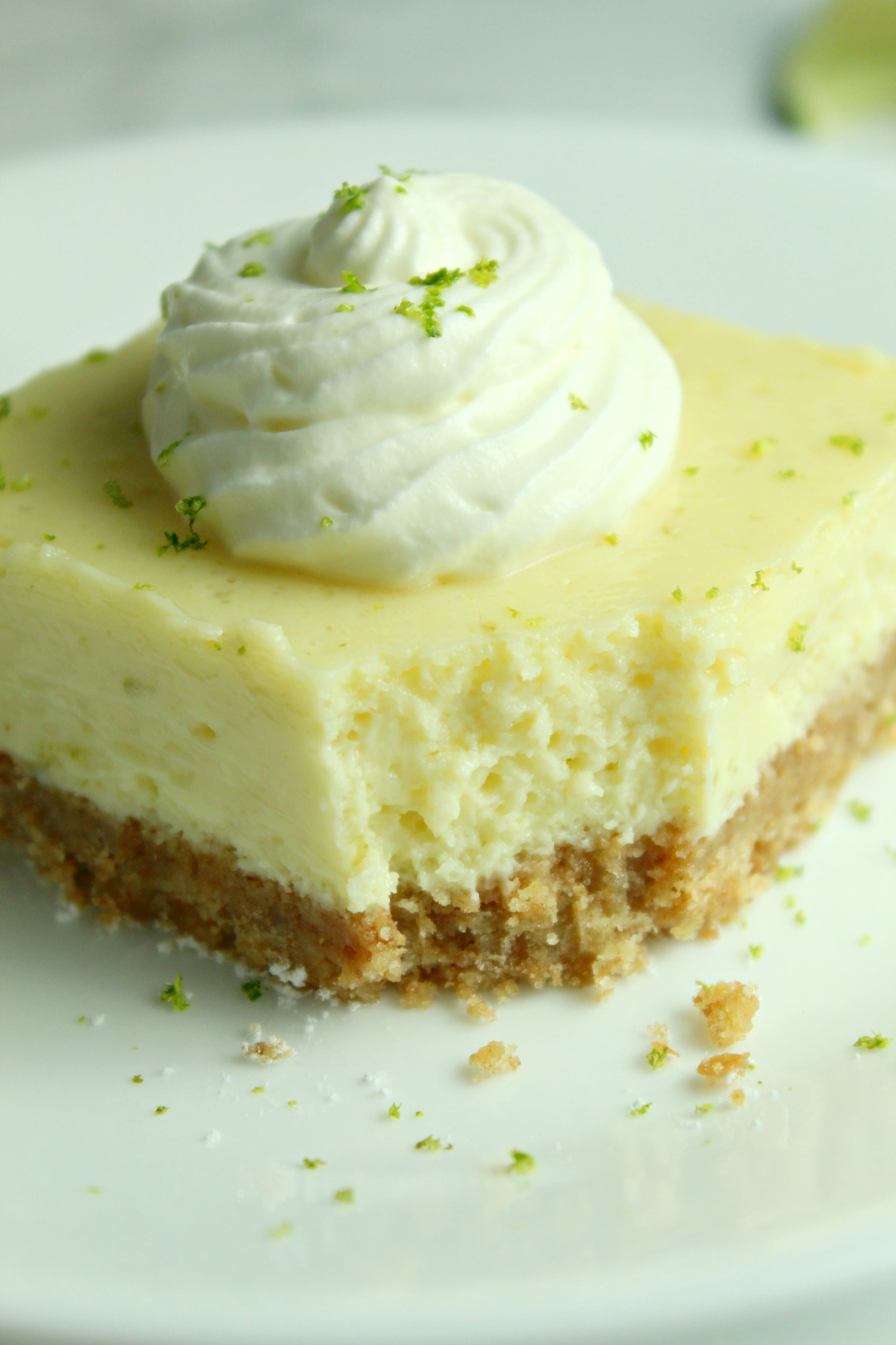 Key Lime Bars with lime whipped cream topped with lime zest on a white plate with a bite taken out