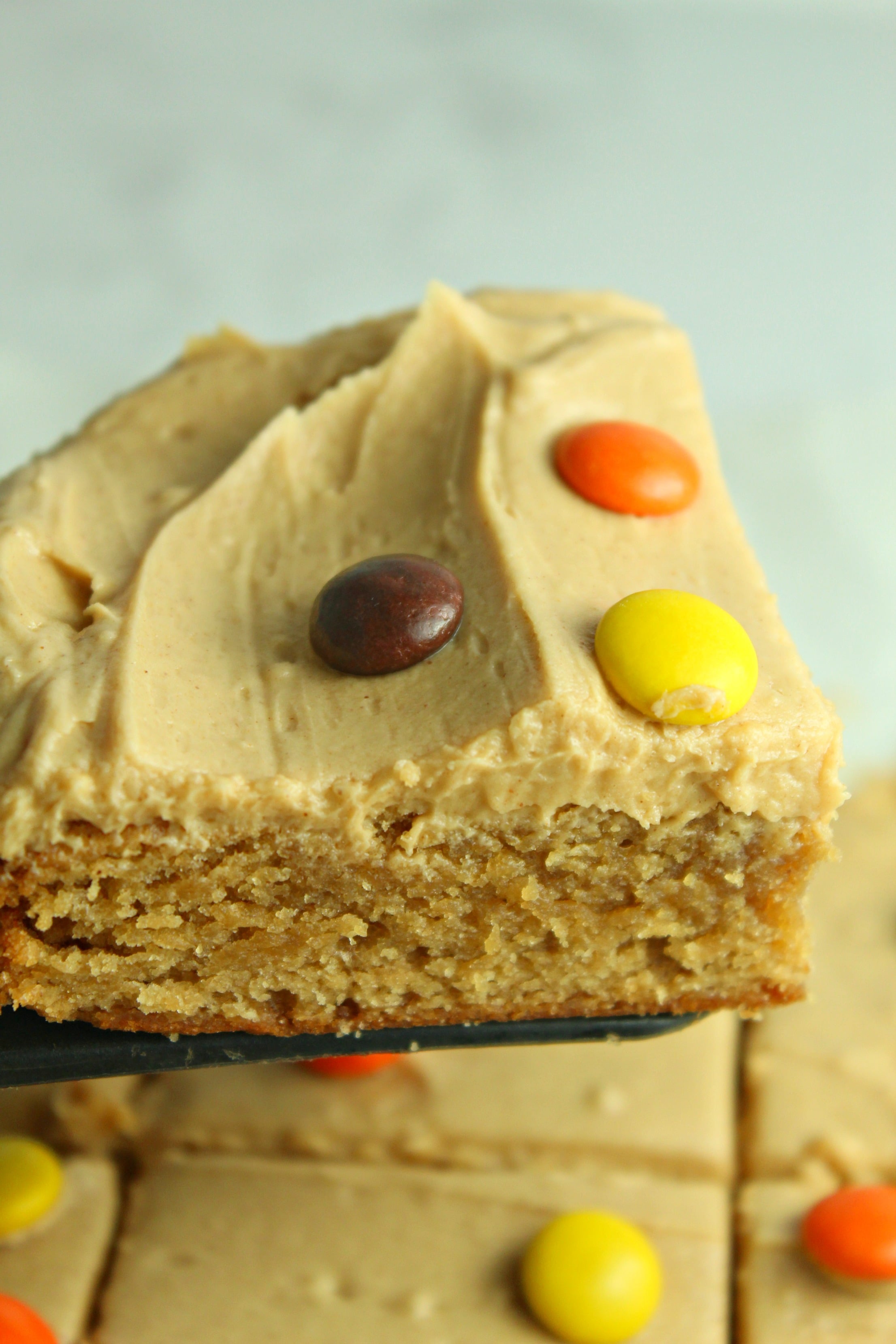 Peanut Butter Bars topped with peanut butter frosting & reeses pieces being lifted out of the pan