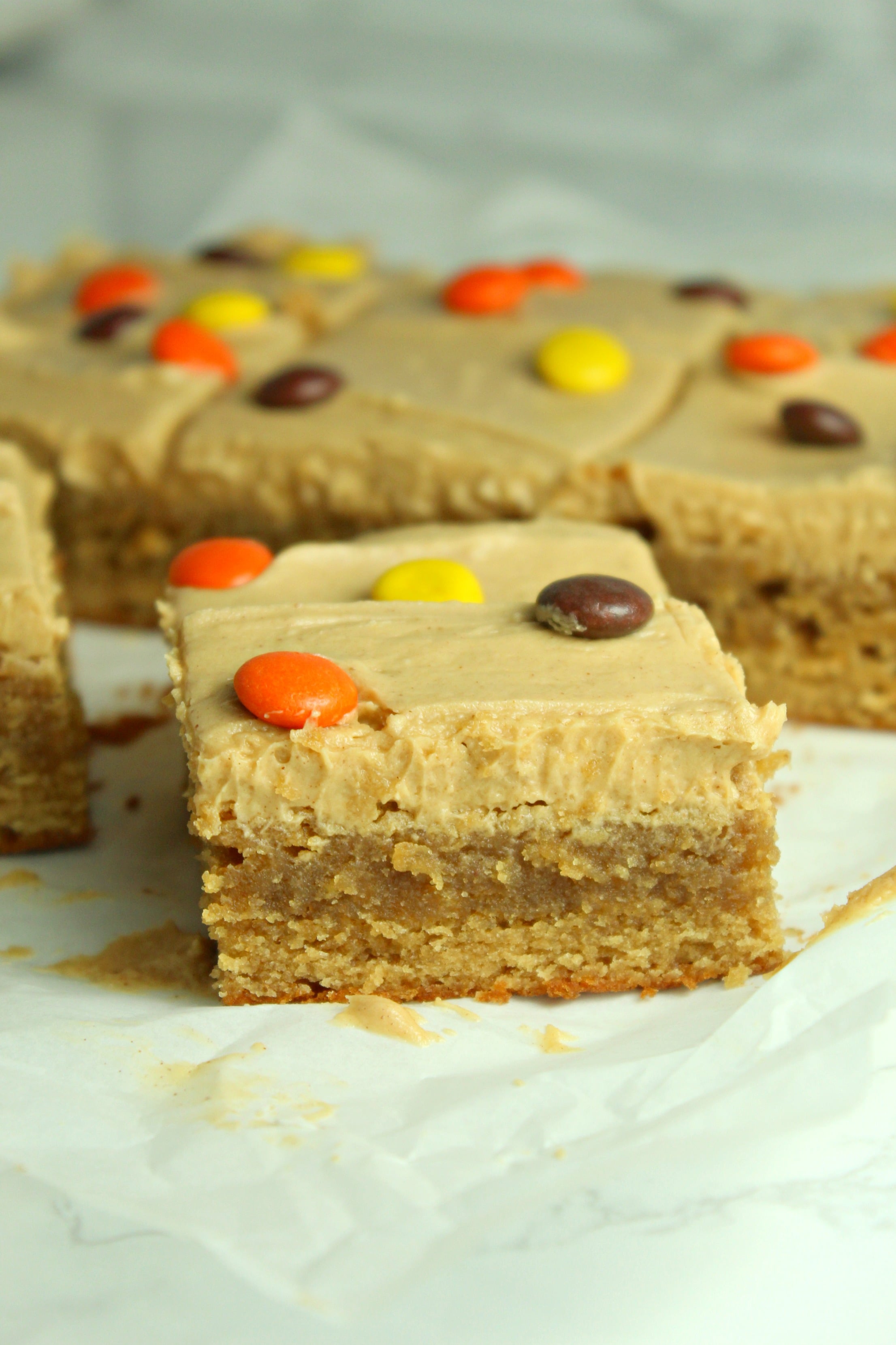 Peanut Butter Bars topped with peanut butter frosting & reeses pieces on a white table