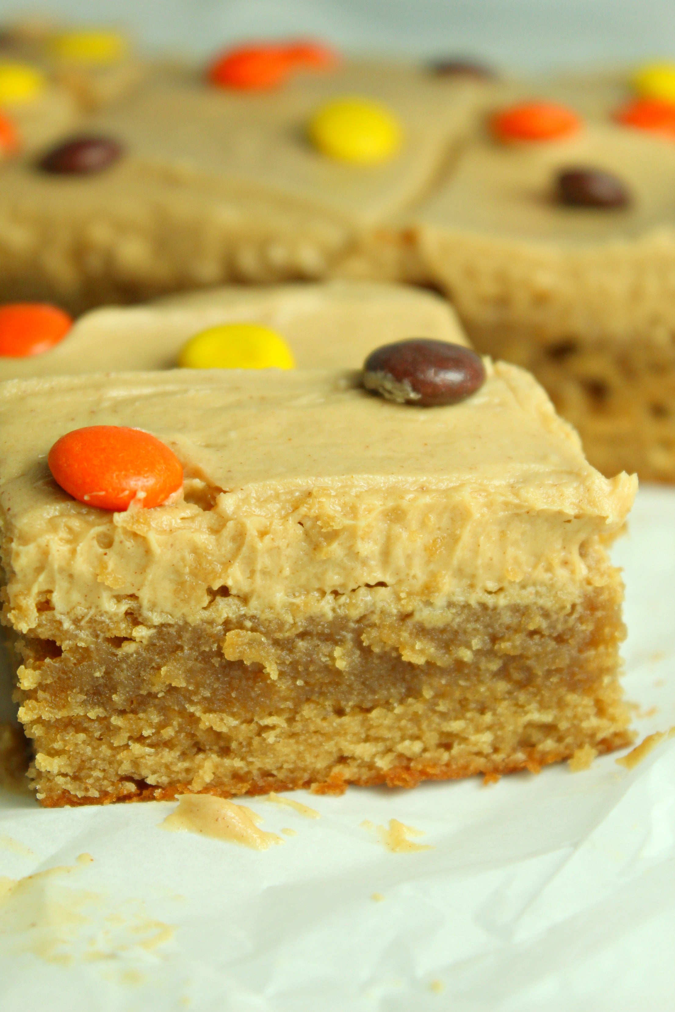 Peanut Butter Bars topped with peanut butter frosting & reeses pieces on a white table