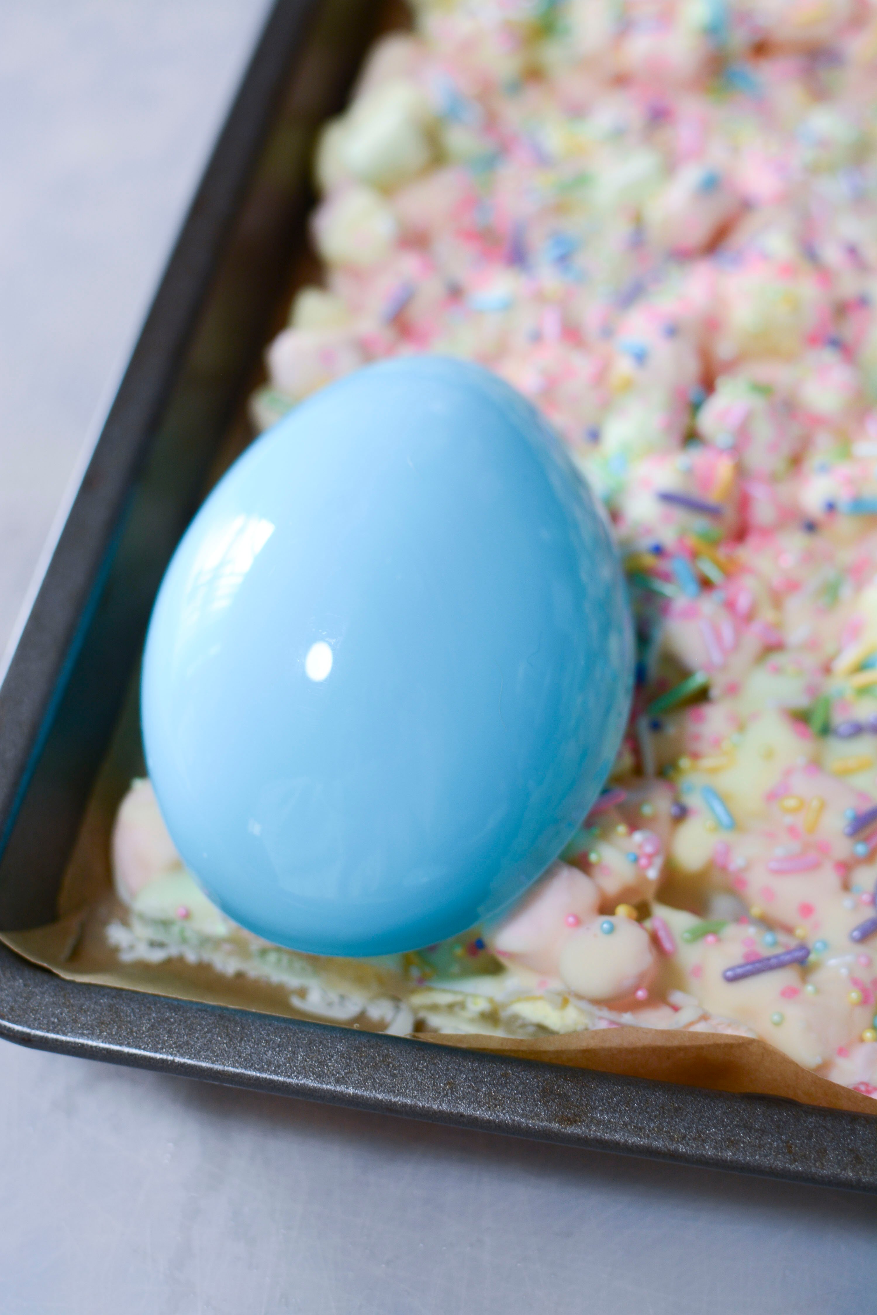 Easter Marshmallow treats with pink, green and yellow mini marshmallows on a cookie sheet with a plastic egg cutting out a treat