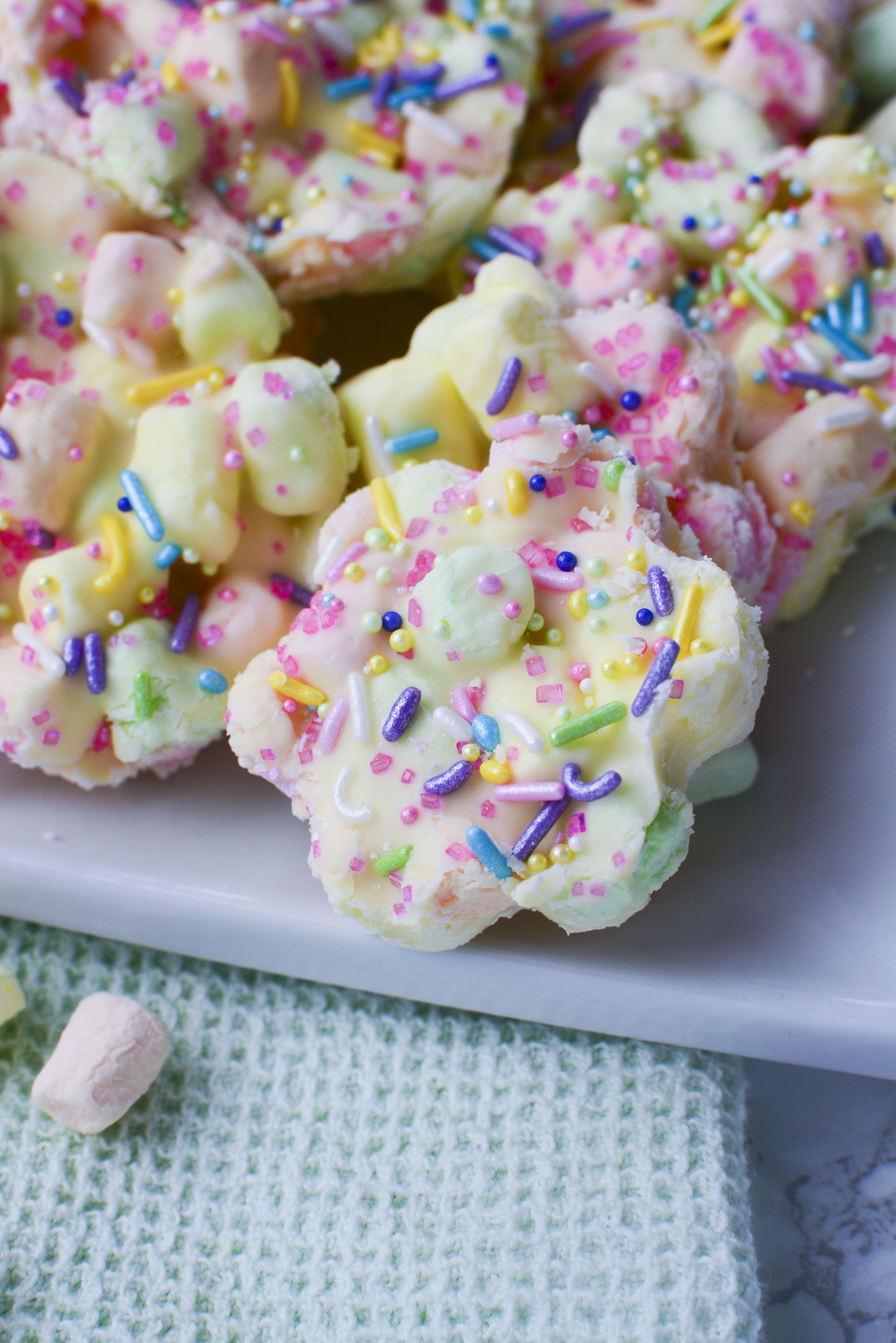 Easter Marshmallow treats with pink, green and yellow mini marshmallows cut into the shape of flowers on a square white plate
