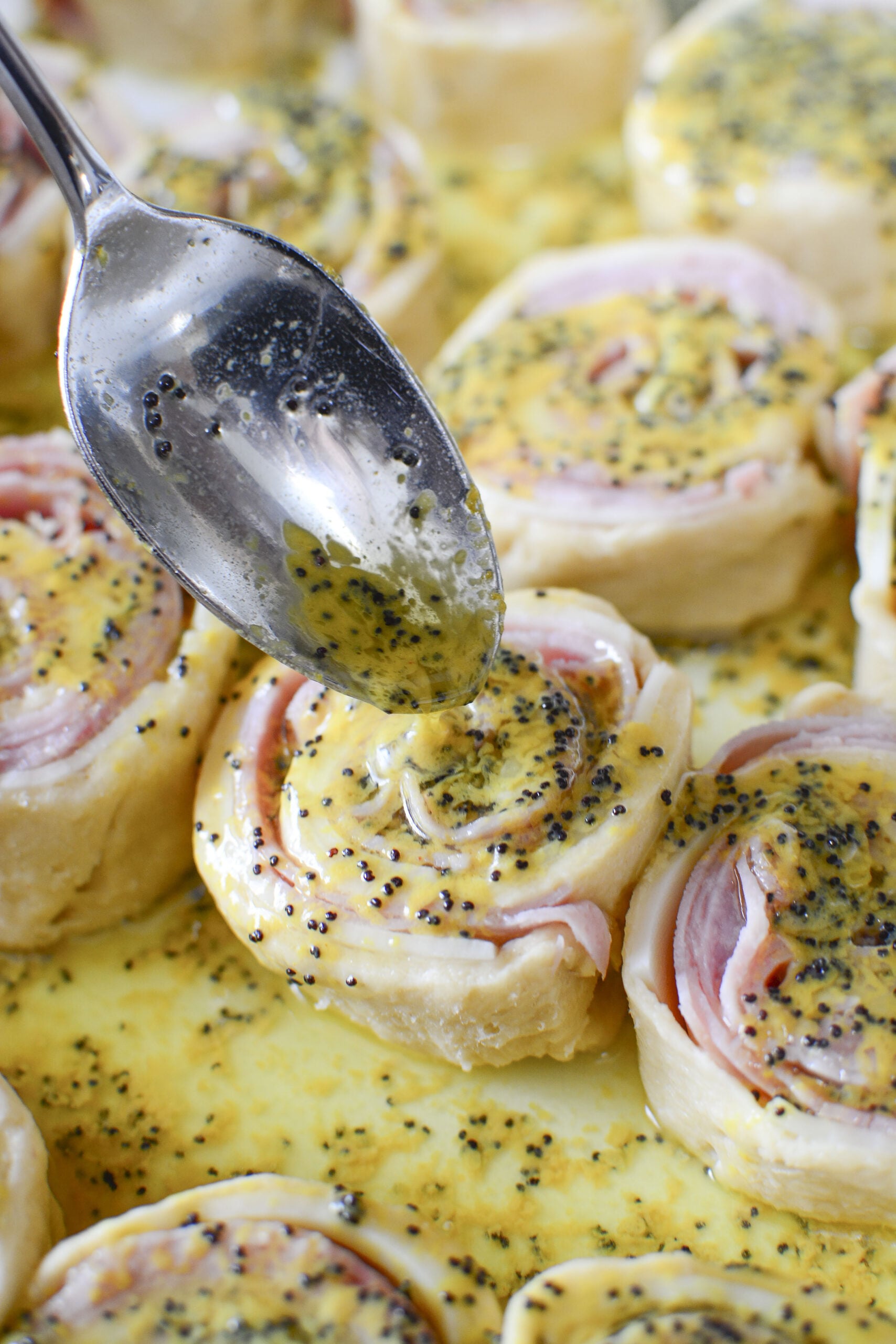 Ham and Cheese Pinwheels uncooked with dijon sauce being poured on top