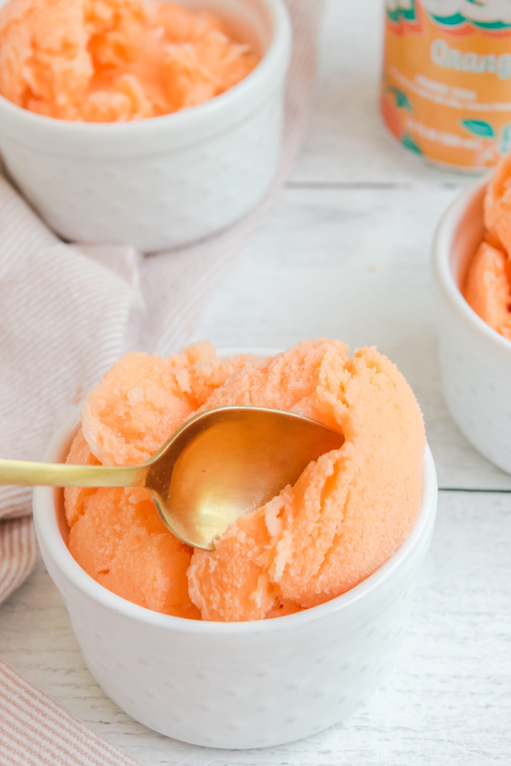 Orange Crush Sherbet in a white bowl with a gold spoon digging in