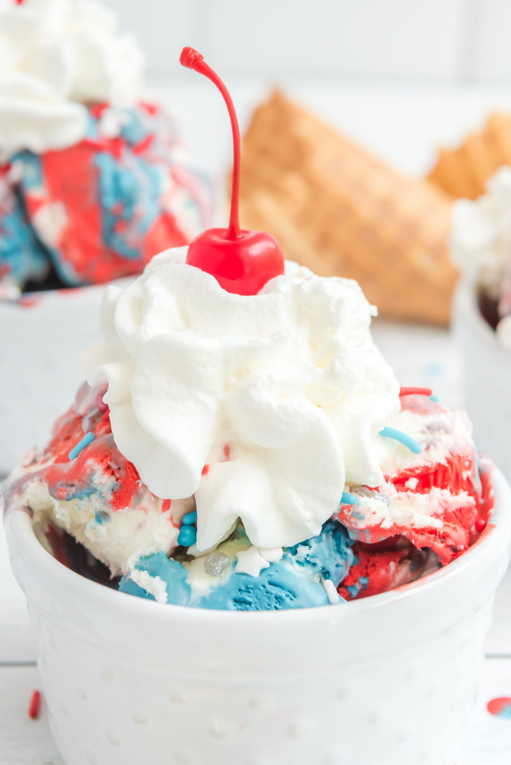 Red, White & Blue Ice Cream in a white bowl topped with whipped cream and a cherry
