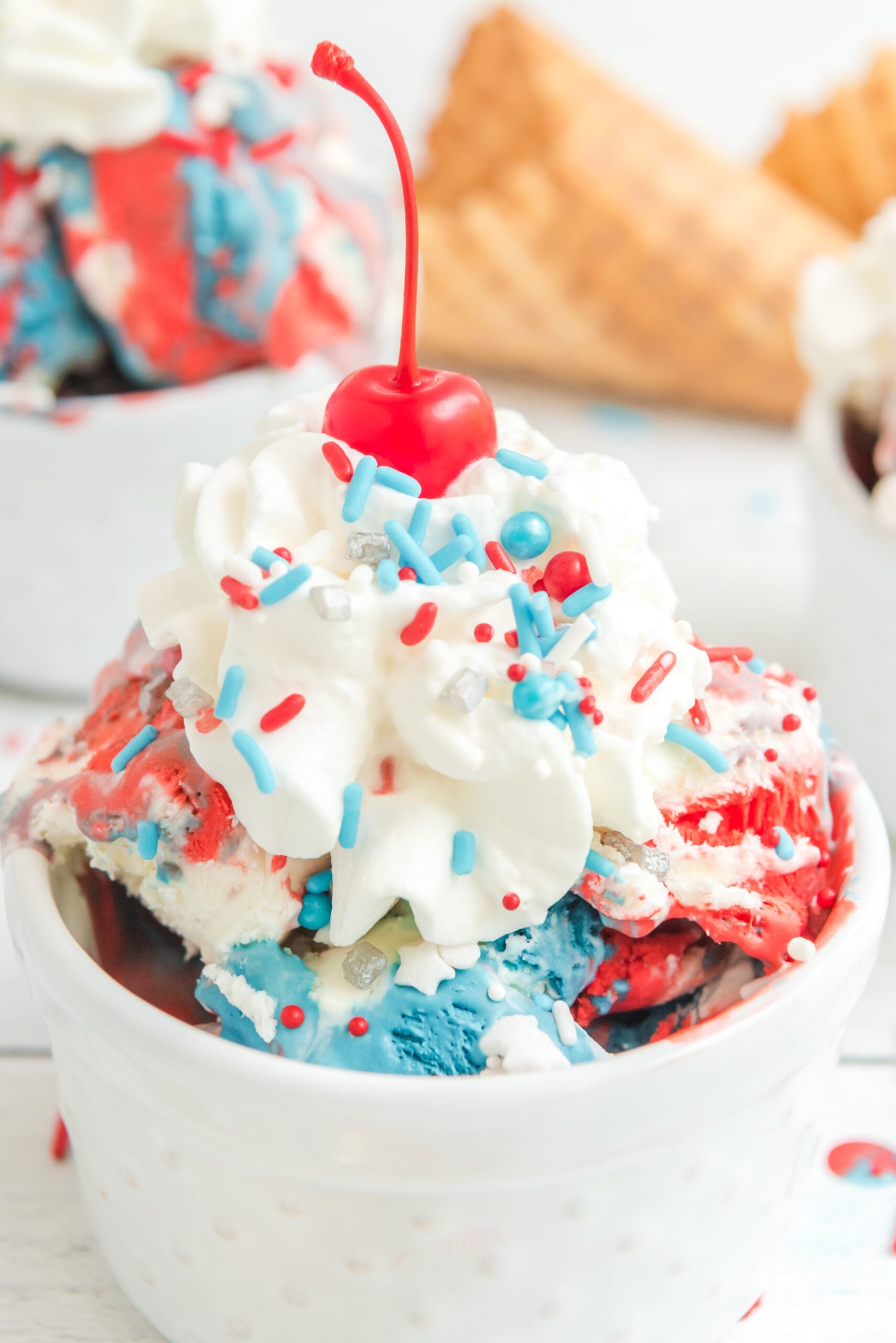 Red, White & Blue Ice Cream in a white bowl topped with whipped cream and a cherry