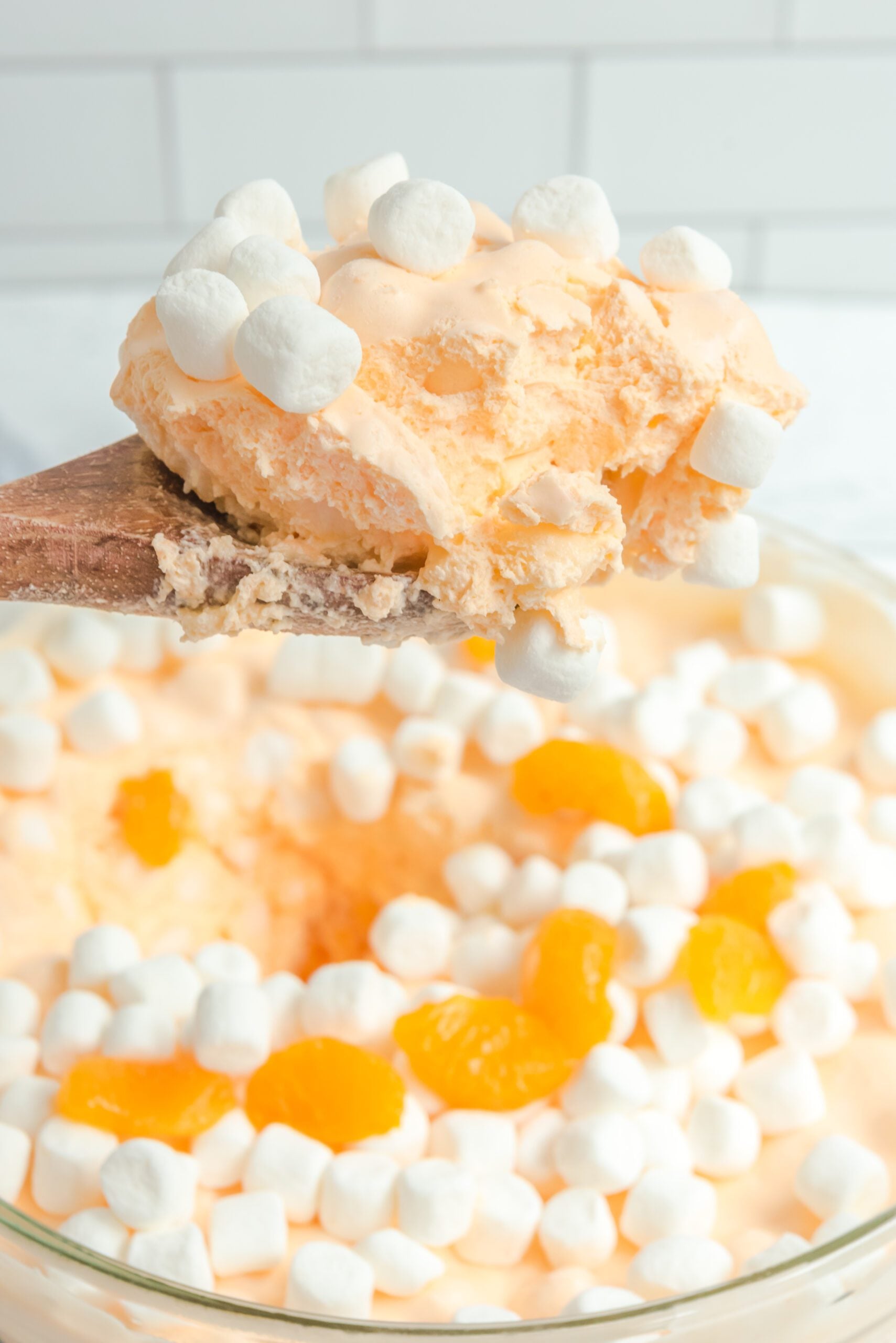 Orange Creamsicle Salad in a serving bowl with a wodden spoon lifting up a scoop