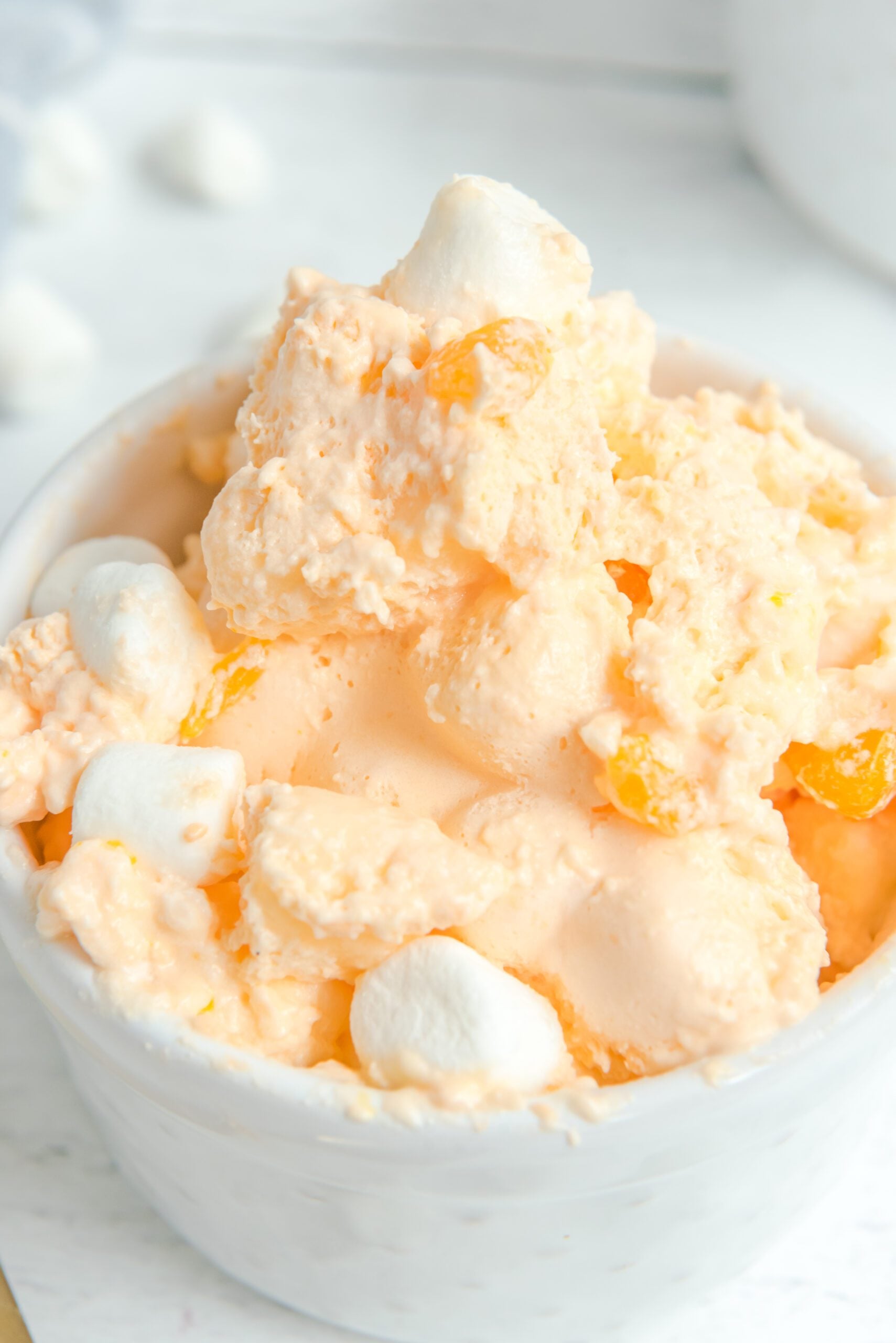 Orange Creamsicle Salad in a white bowl topped with marshmallows and mandarin oranges extreme close up shot