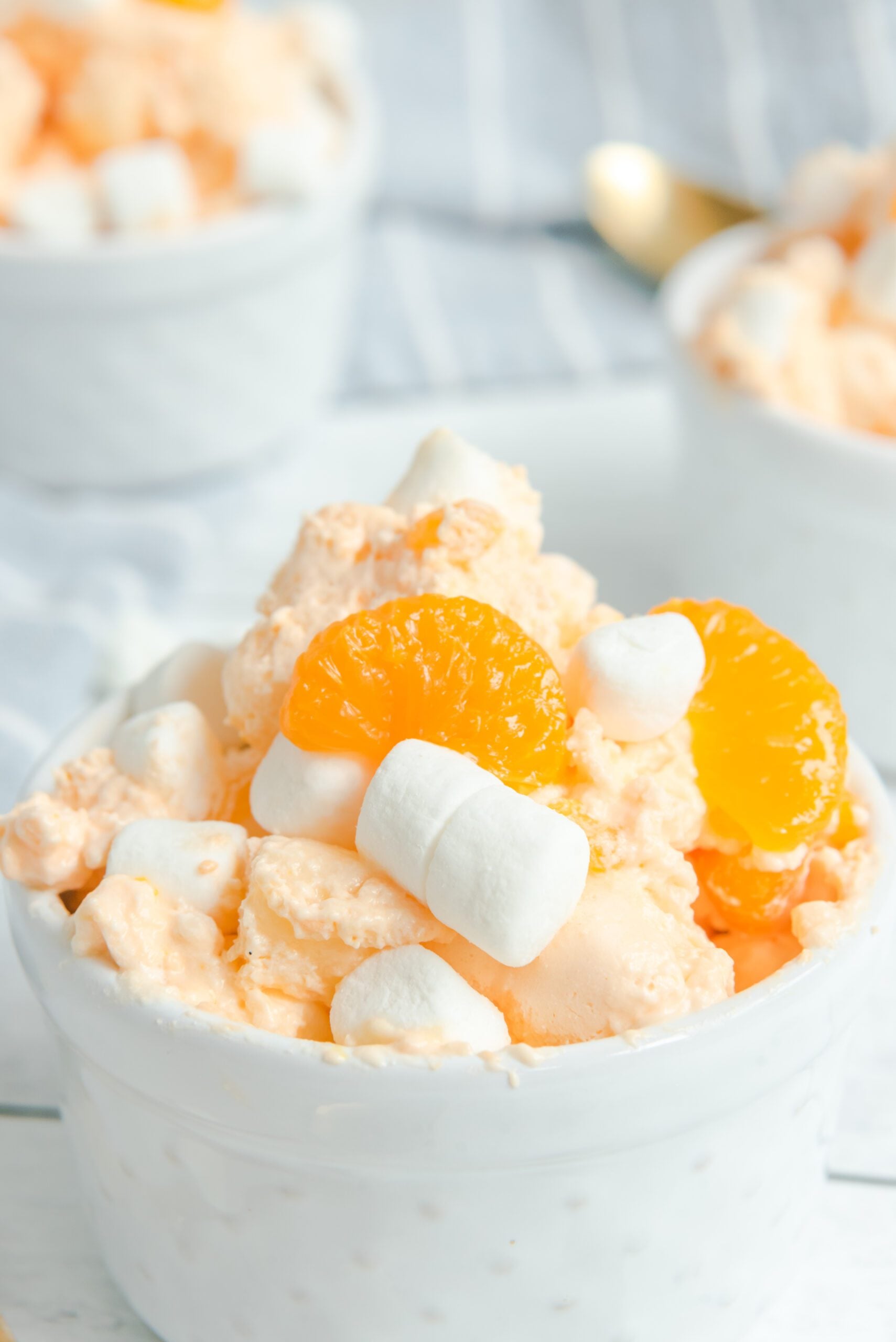 Orange Creamsicle Salad in a white bowl topped with marshmallows and mandarin oranges close up shot