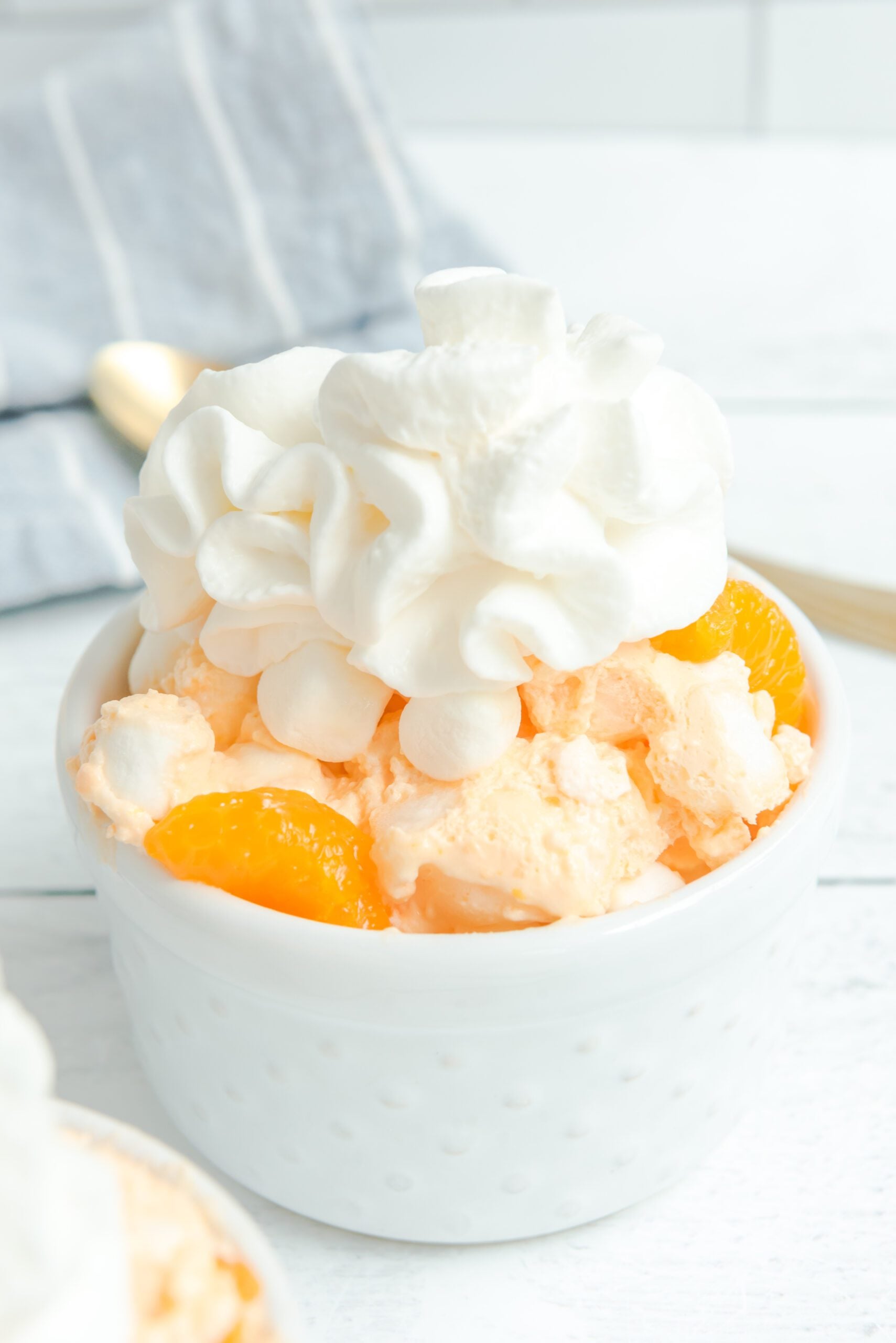 Orange Creamsicle Salad in a white bowl topped with whipped cream and mandarin oranges