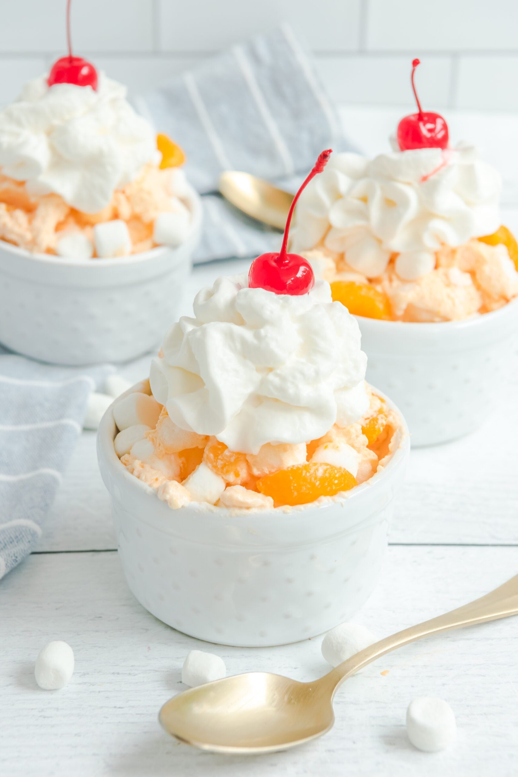 Orange Creamsicle Salad in three white bowls topped with whipped cream and cherries