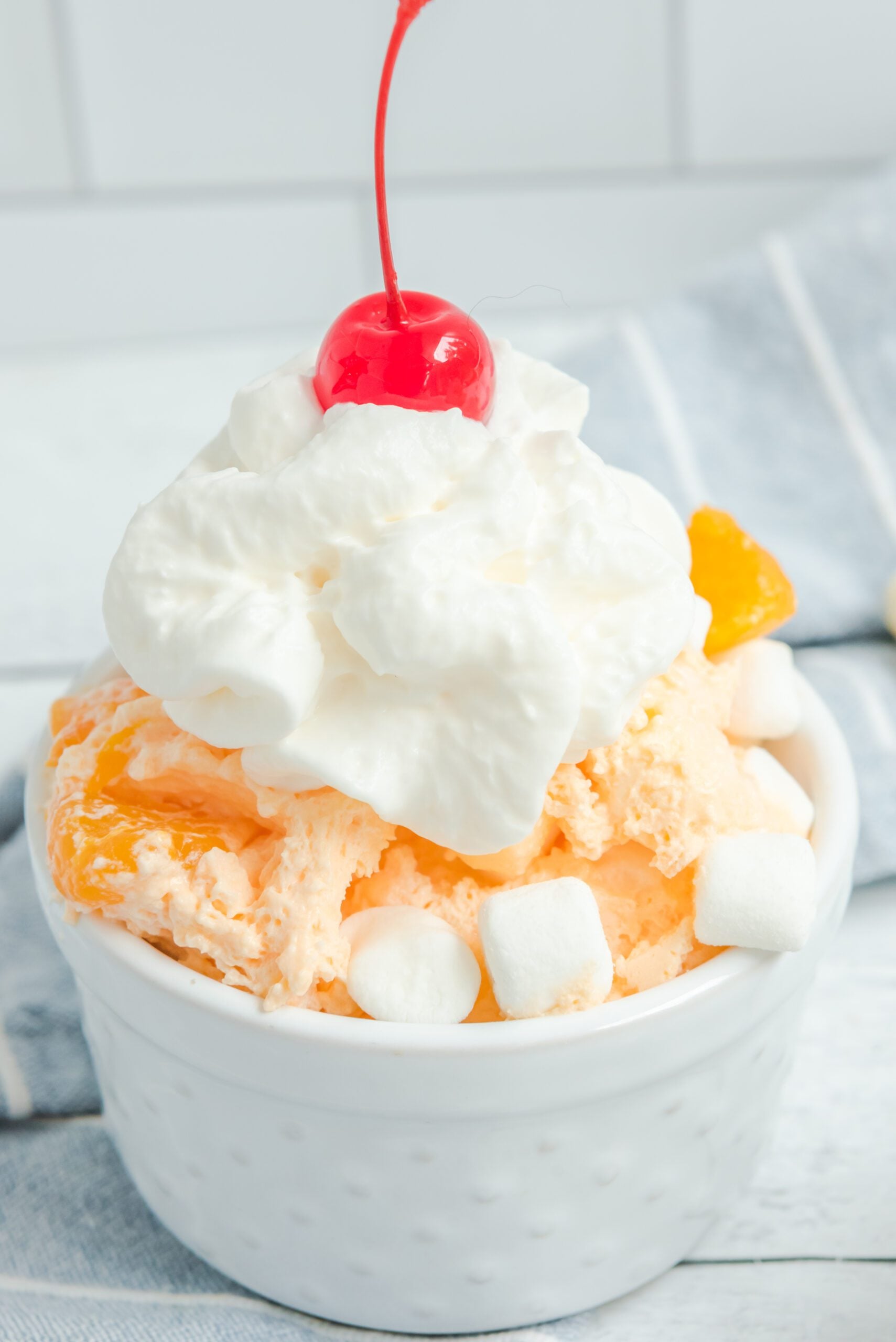 Orange Creamsicle Salad in a white bowl topped with whipped cream and a cherry