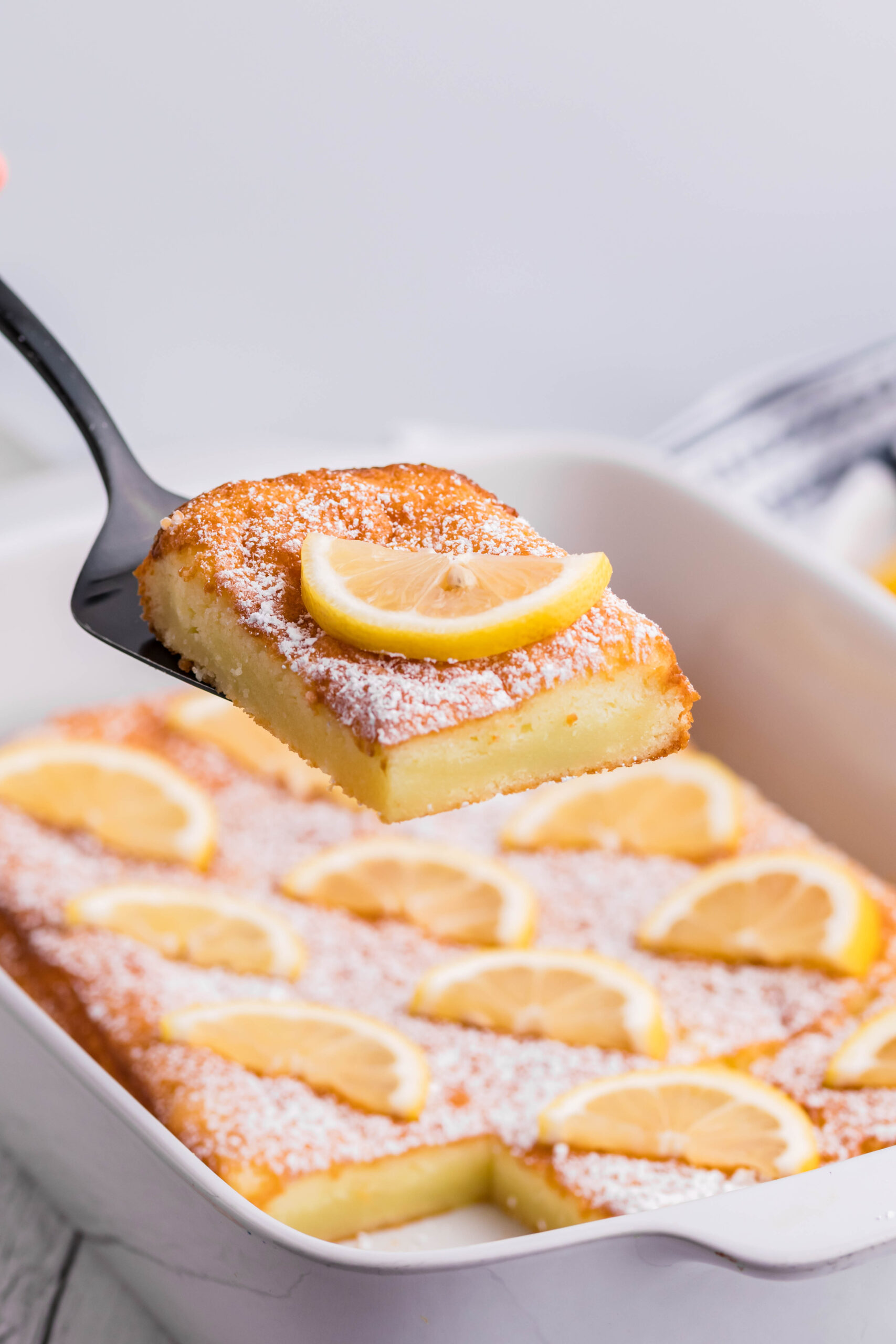 2 Ingredient Lemon Bars in a white baking pan with a slice being lifted on a spatula