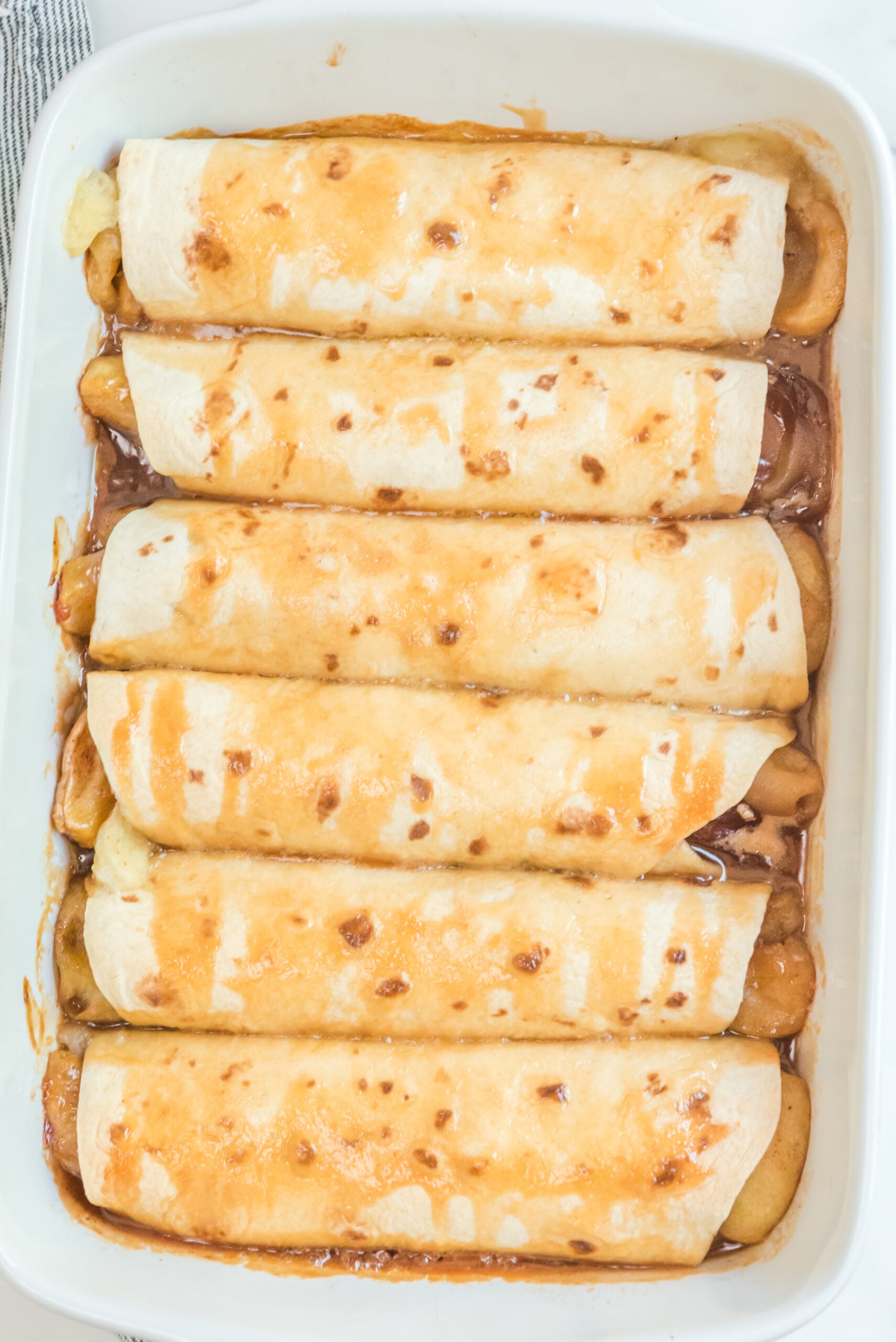 Apple Pie Enchiladas topped with caramel sauce in a white baking dish overhead shot