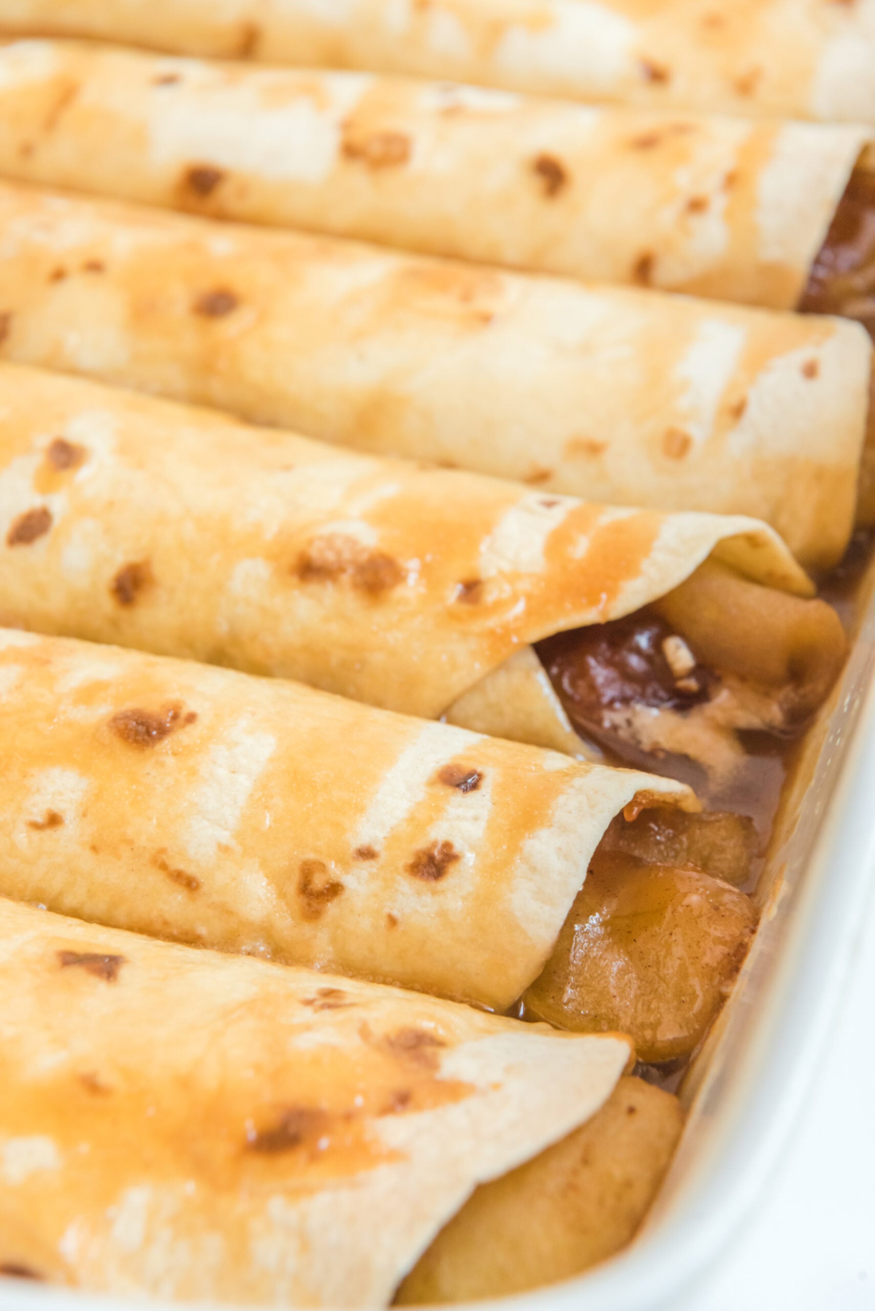 Apple Pie Enchiladas topped with caramel sauce in a white baking dish
