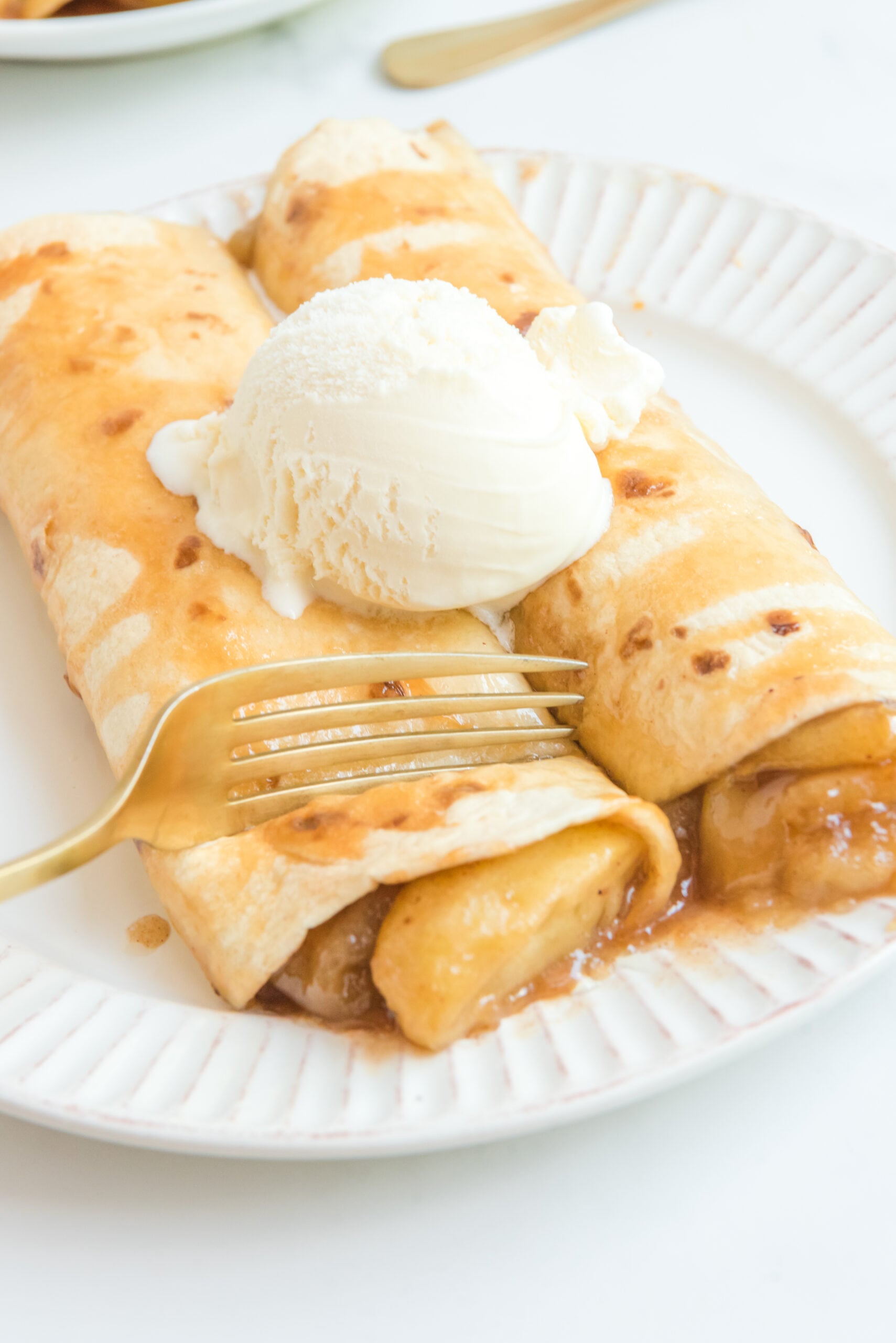 Apple Pie Enchiladas topped with vanilla ice cream with a fork slicing into it