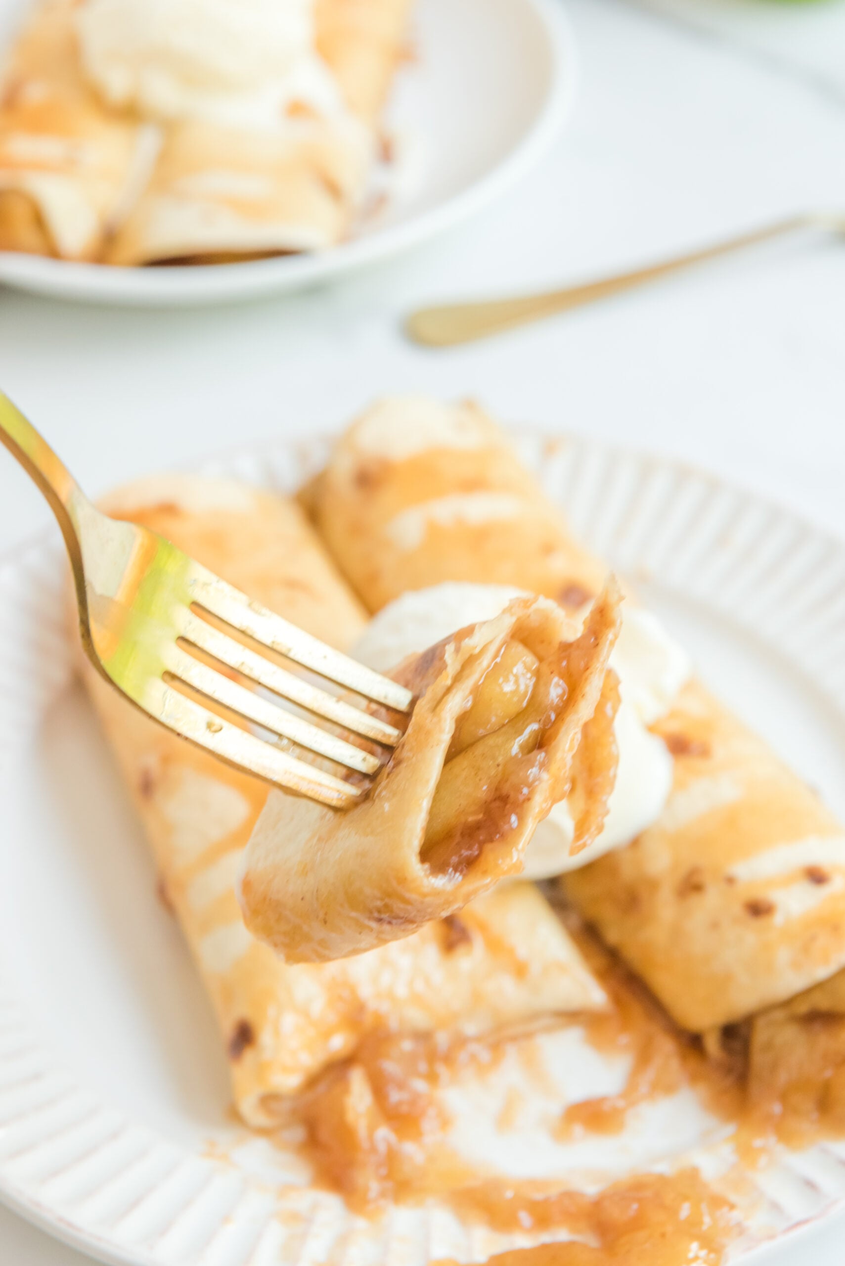 Apple Pie Enchiladas topped with vanilla ice cream with a bite being lifted on a fork