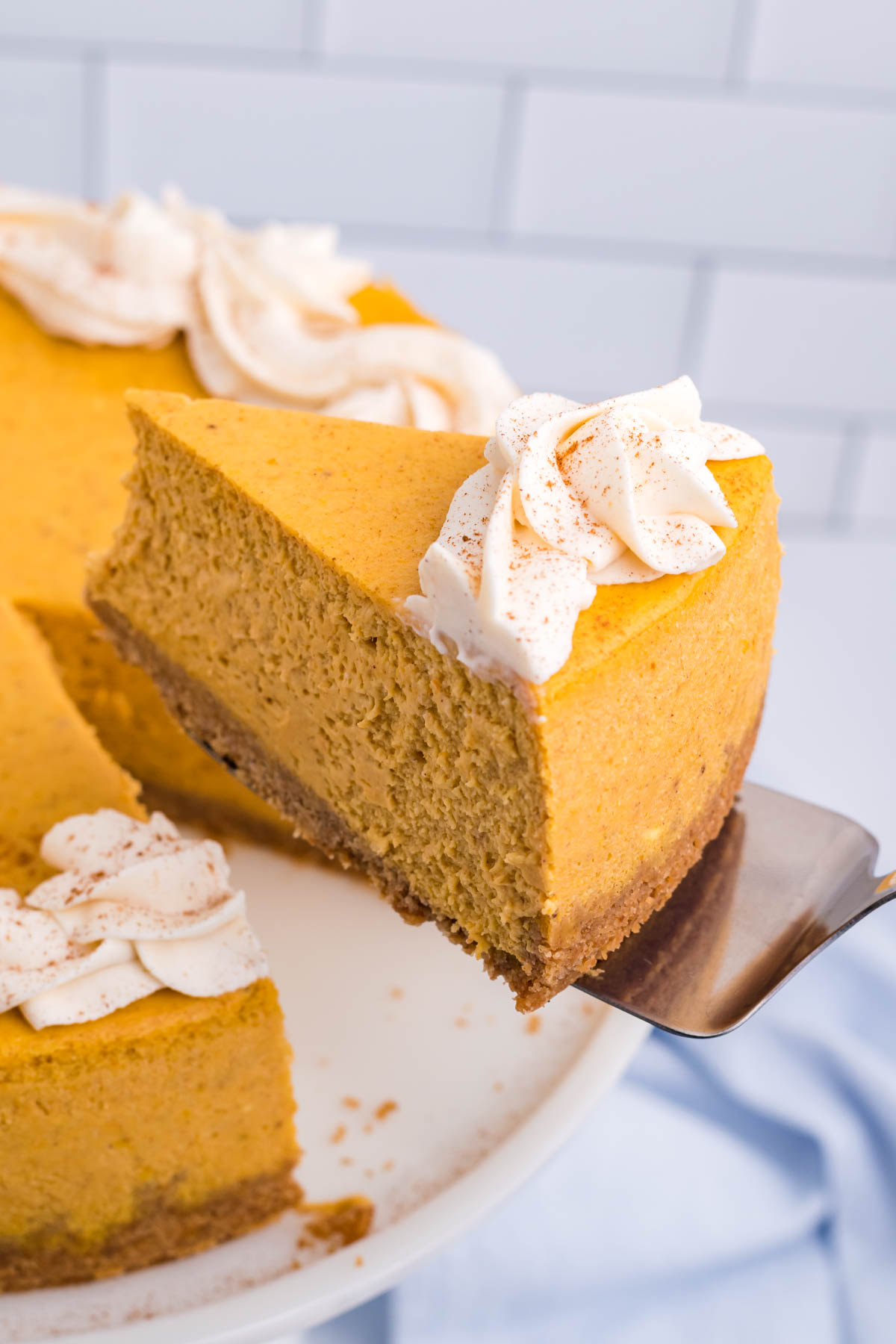 Pumpkin Cheesecake on a white cake stand with a spatula lifting out a slice