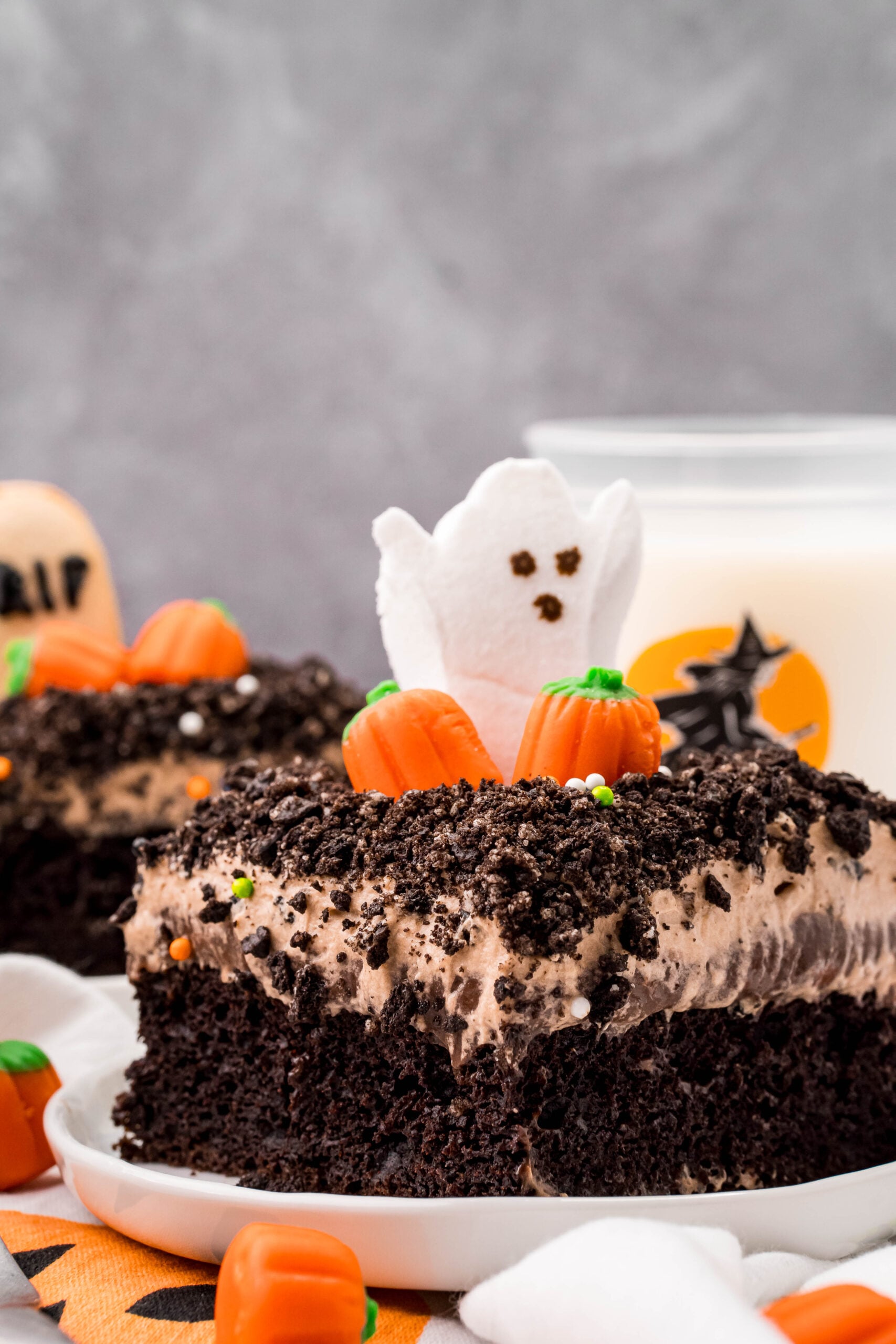 Halloween Dirt Cake slice on a white plate with a glass of milk in the background