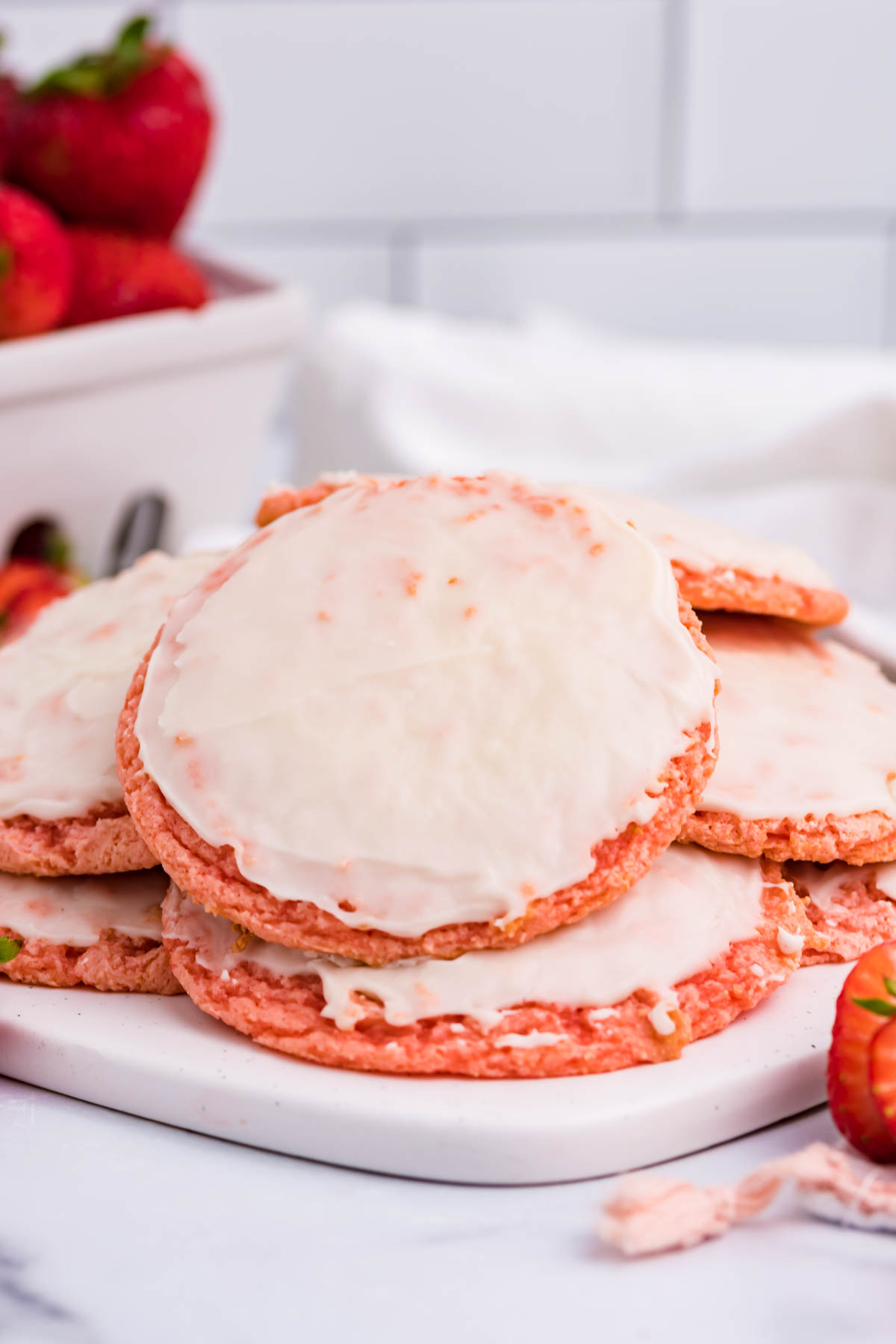 Strawberry Cool Whip Cookies with a container of strawberries in the background on a white plate