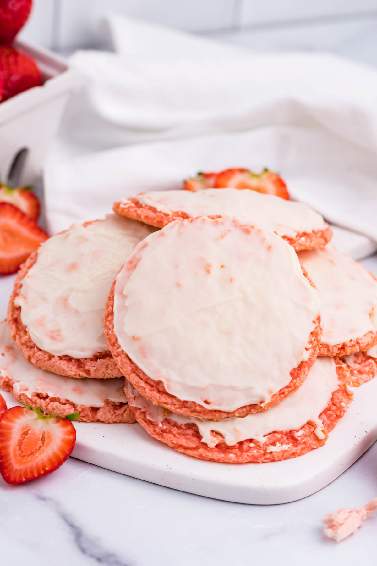 Strawberry Cool Whip Cookies piled on a white plate and surrounded by sliced strawberries