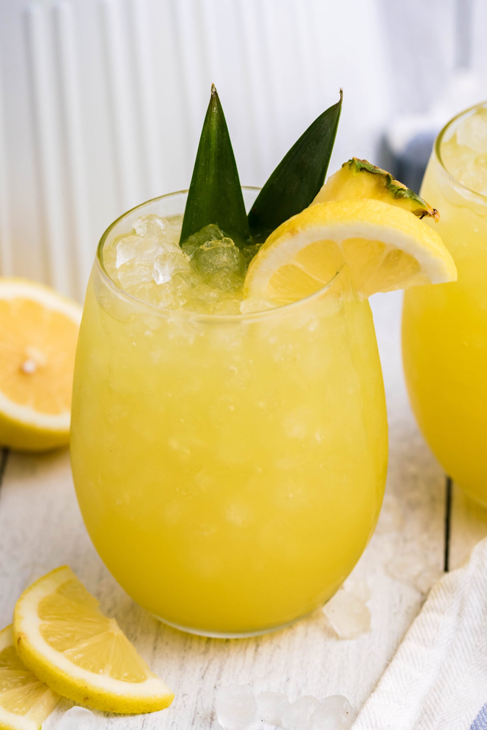 Pineapple Lemonade in a clear glass with pineapple leaves and a sliced lemon in the glass
