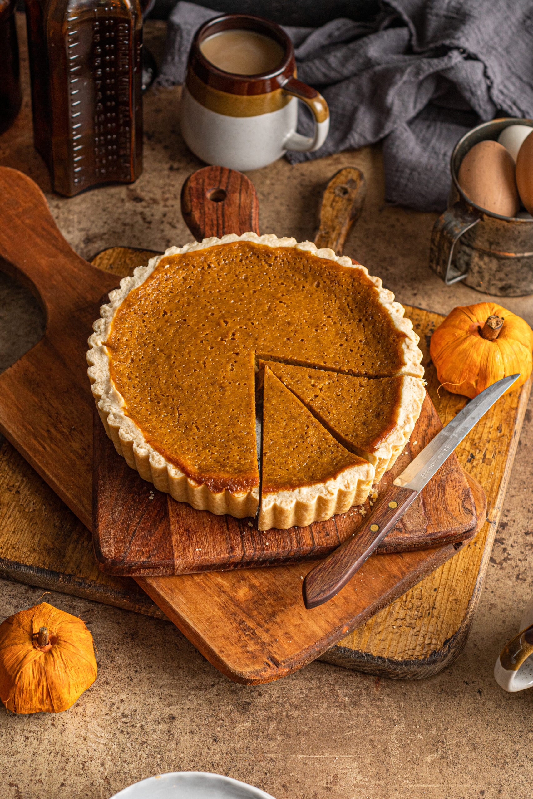 Pumpkin Pie Tart on a wooden cutting board with coffee in a mug and little pumpkins