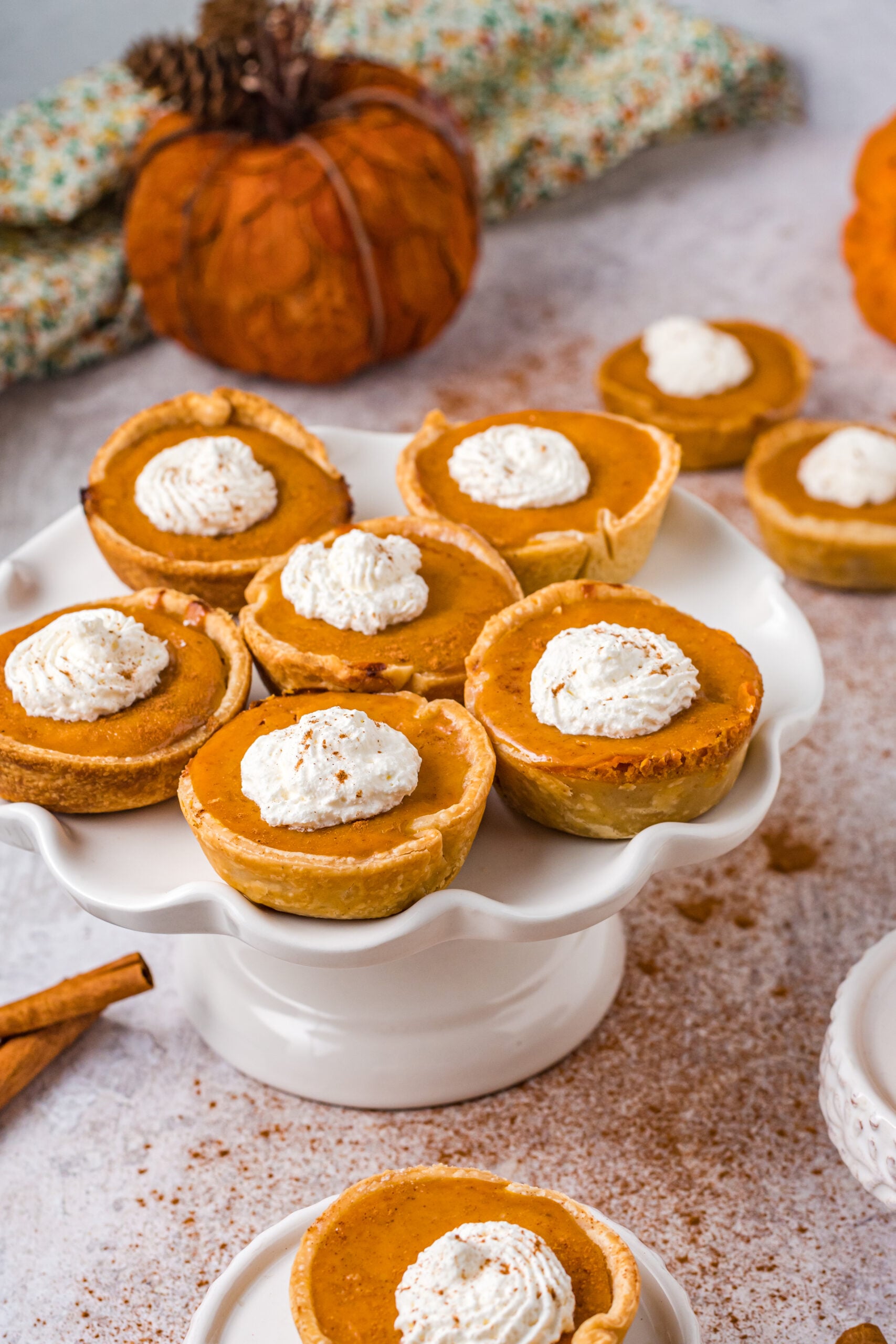 Mini Pumpkin Pies on a white cake stand all topped with dollops of whipped cream 