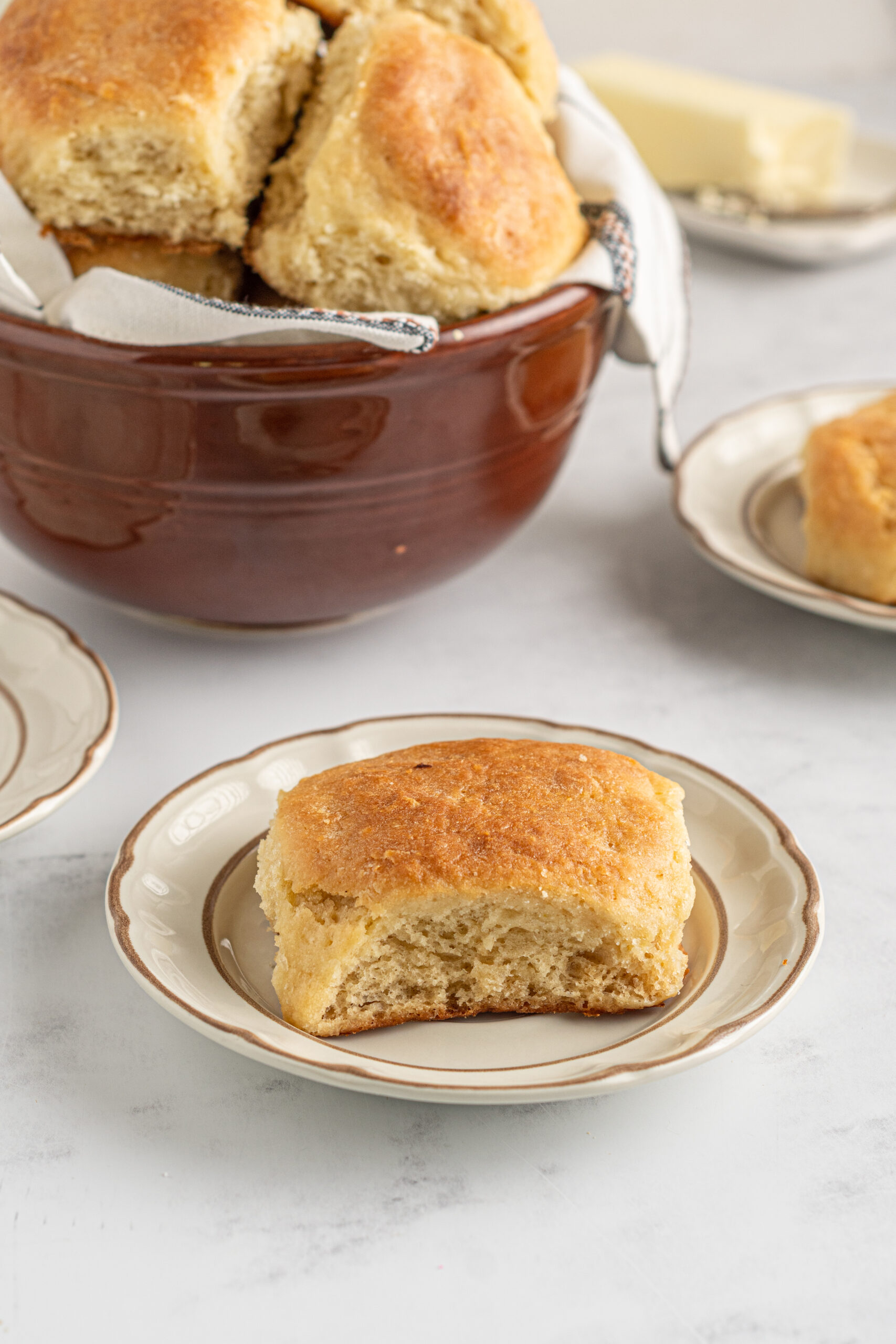 A biscuit on a tan and brown plate with a bowl of biscuits in the background.