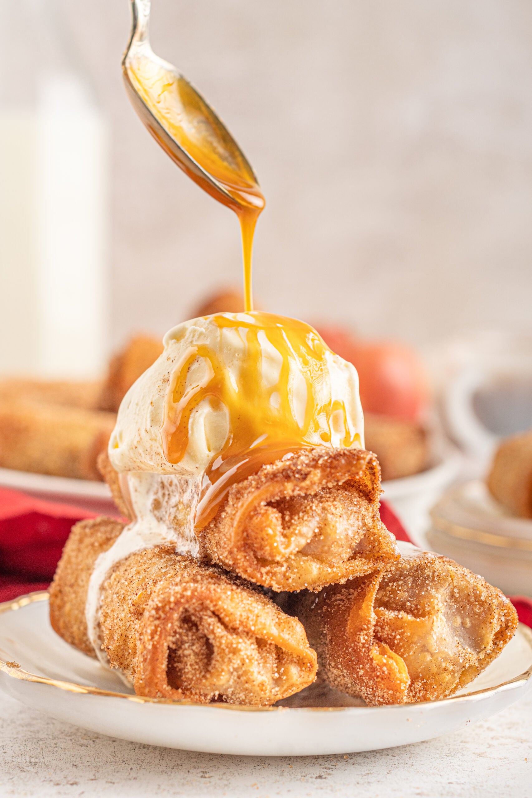 Three Egg Rolls stacked on a white plate with ice cream and caramel sauce on top.