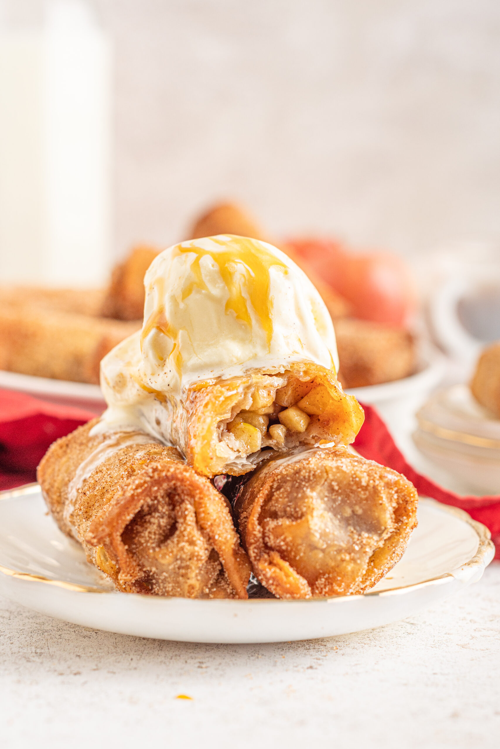 Three Apple Pie Egg Rolls stacked on a white plate with ice cream and caramel sauce on top.