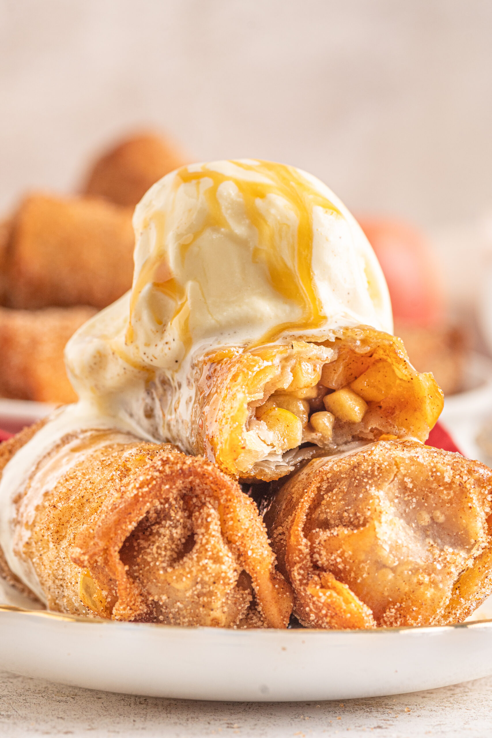 Three Apple Pie Egg Rolls stacked on a white plate with ice cream and caramel sauce on top.