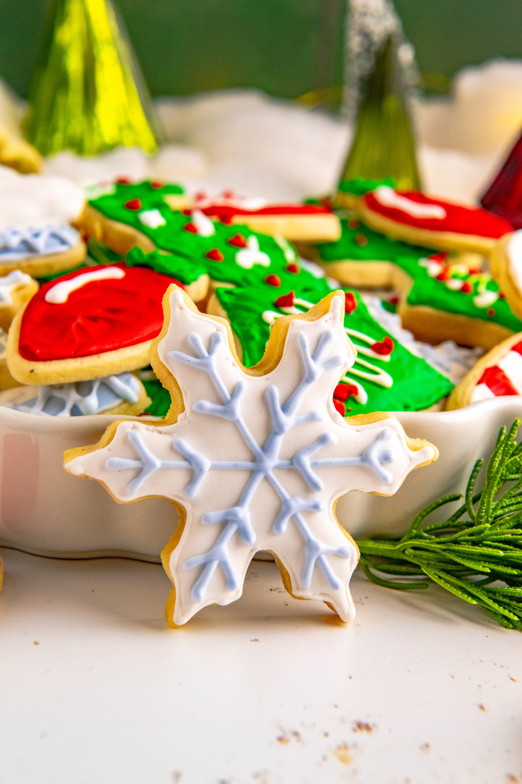 A white and light blue star cookie propped against a white serving tray stacked with Christmas cookies.