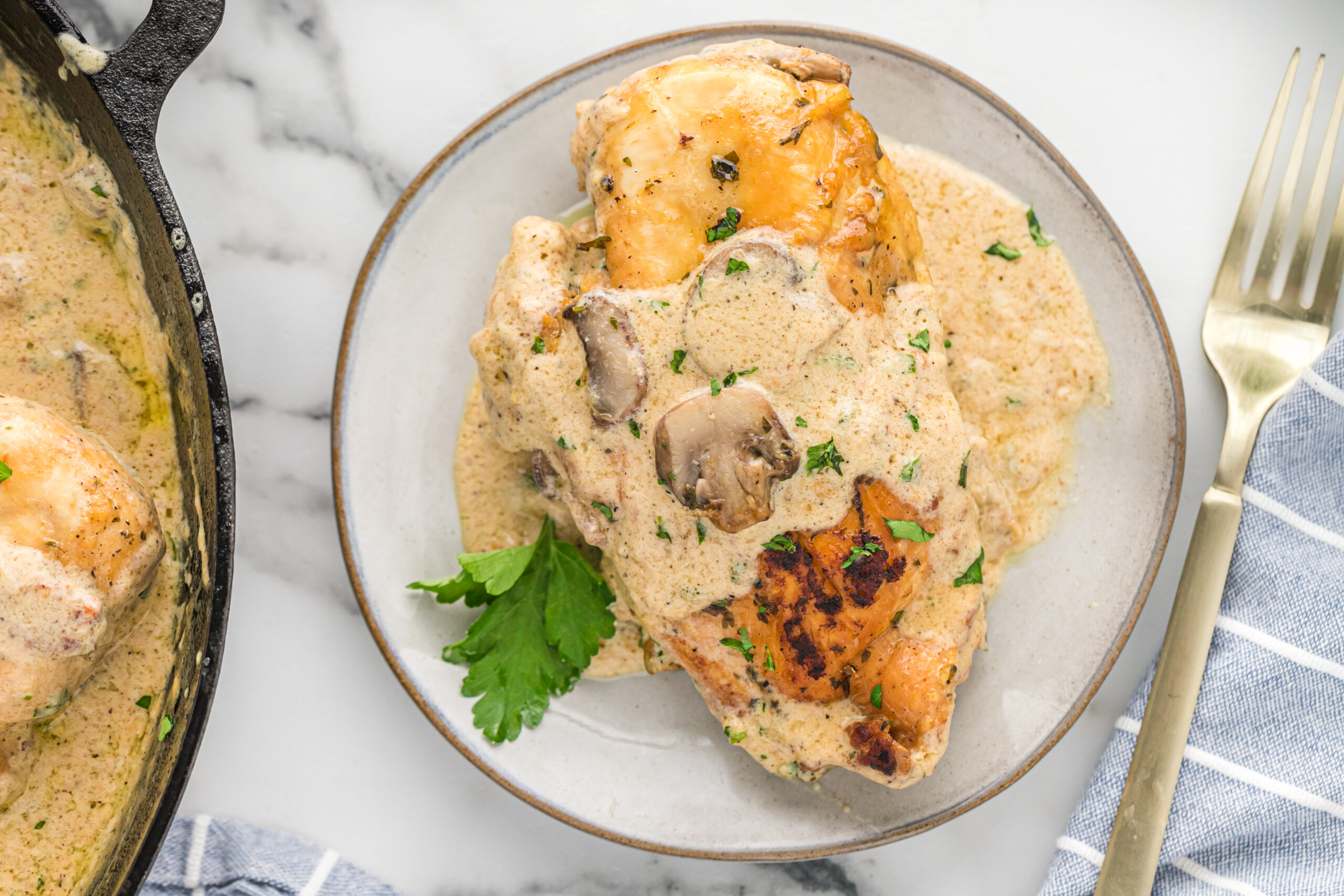 A piece of chicken on a white plate with a gold fork covered in sauce and mushrooms. 