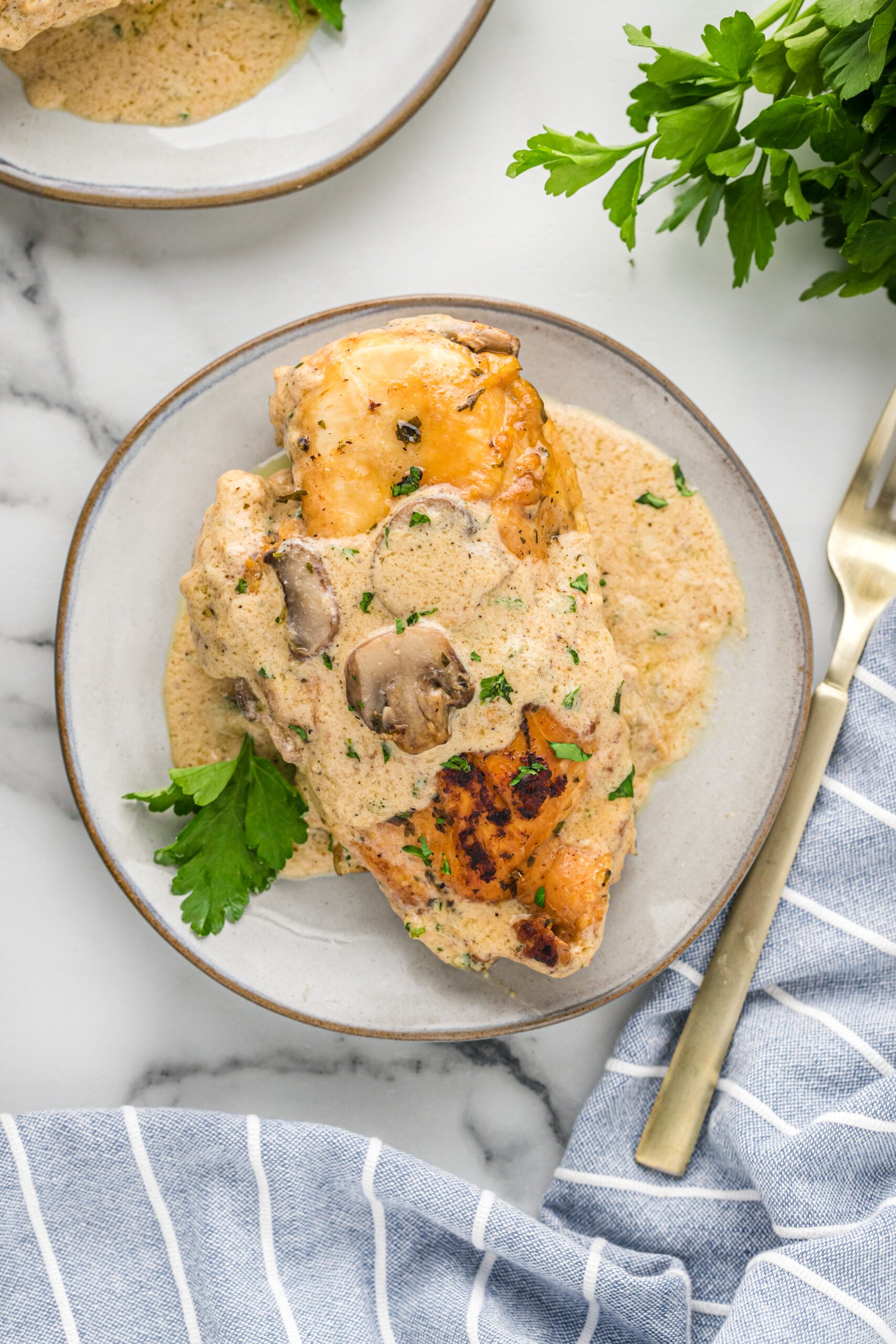 A piece of chicken on a white plate with a gold fork covered in sauce and mushrooms. 