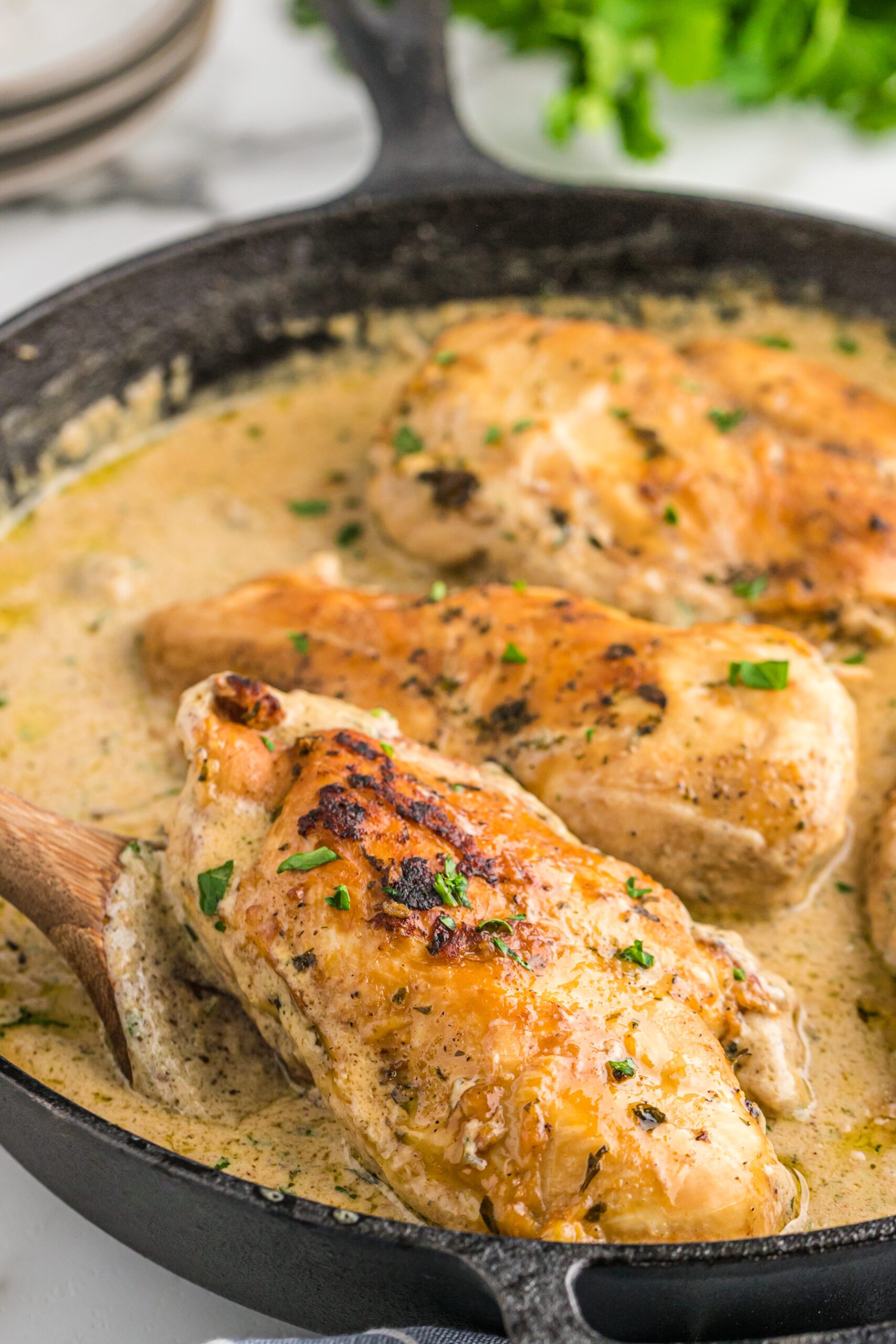 A piece of chicken being lifted from the cast iron skillet using a wooden spatula. 