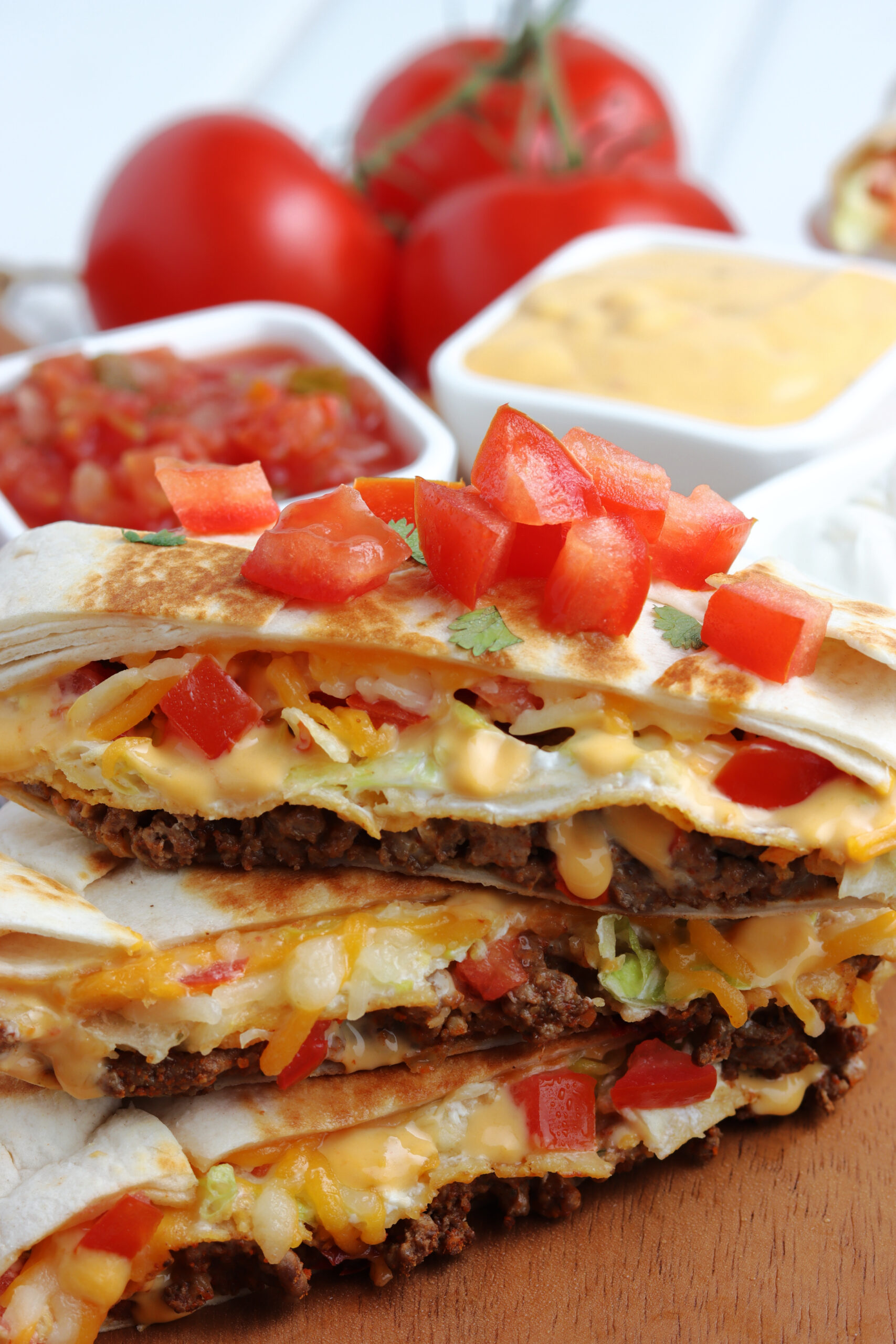 Three crunch wraps cut in half and stacked on top of each other showing the layers on the inside. Topped with cilantro and tomatoes.