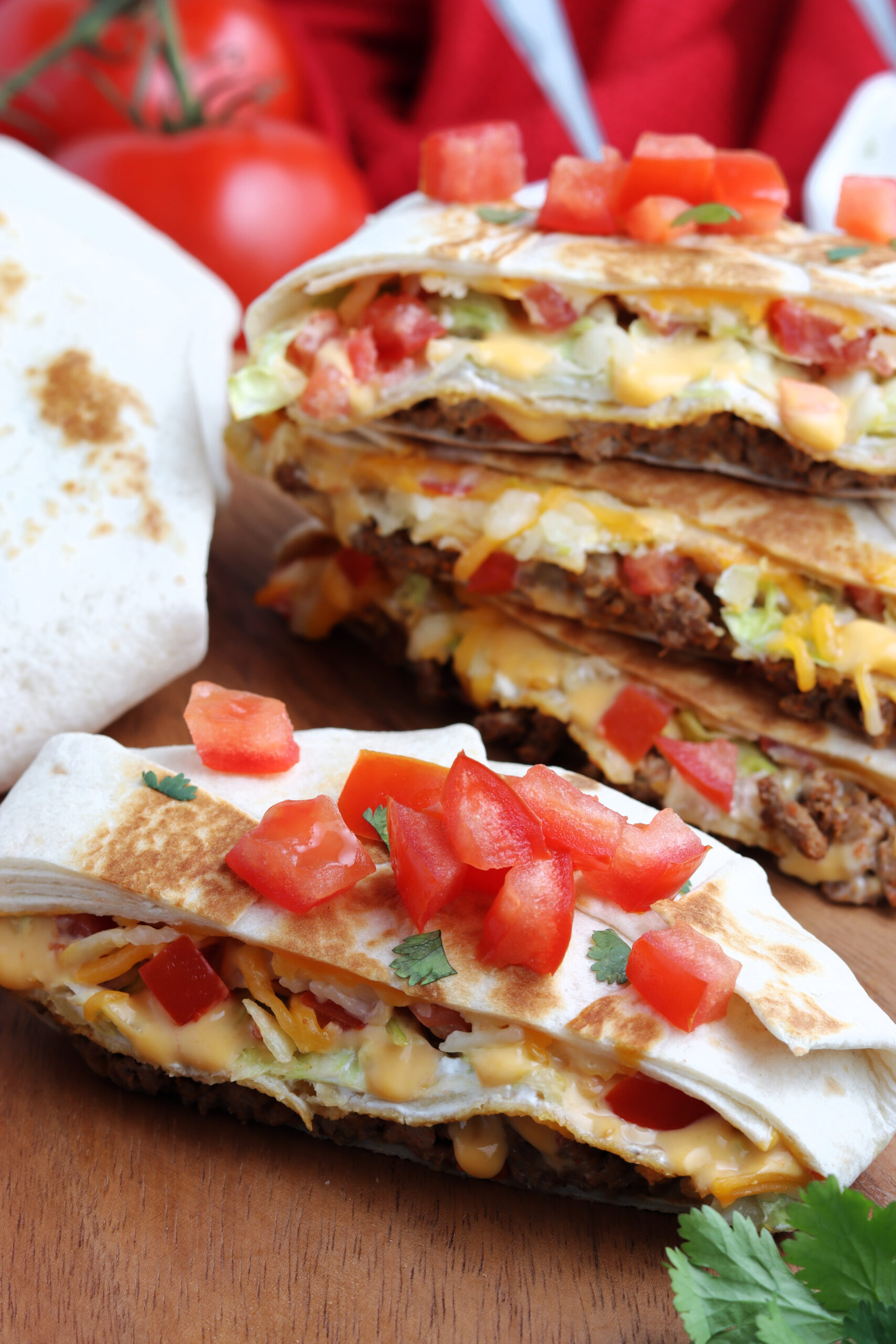 Half of a crunch wrap on a wood board topped with cilantro and tomatoes.