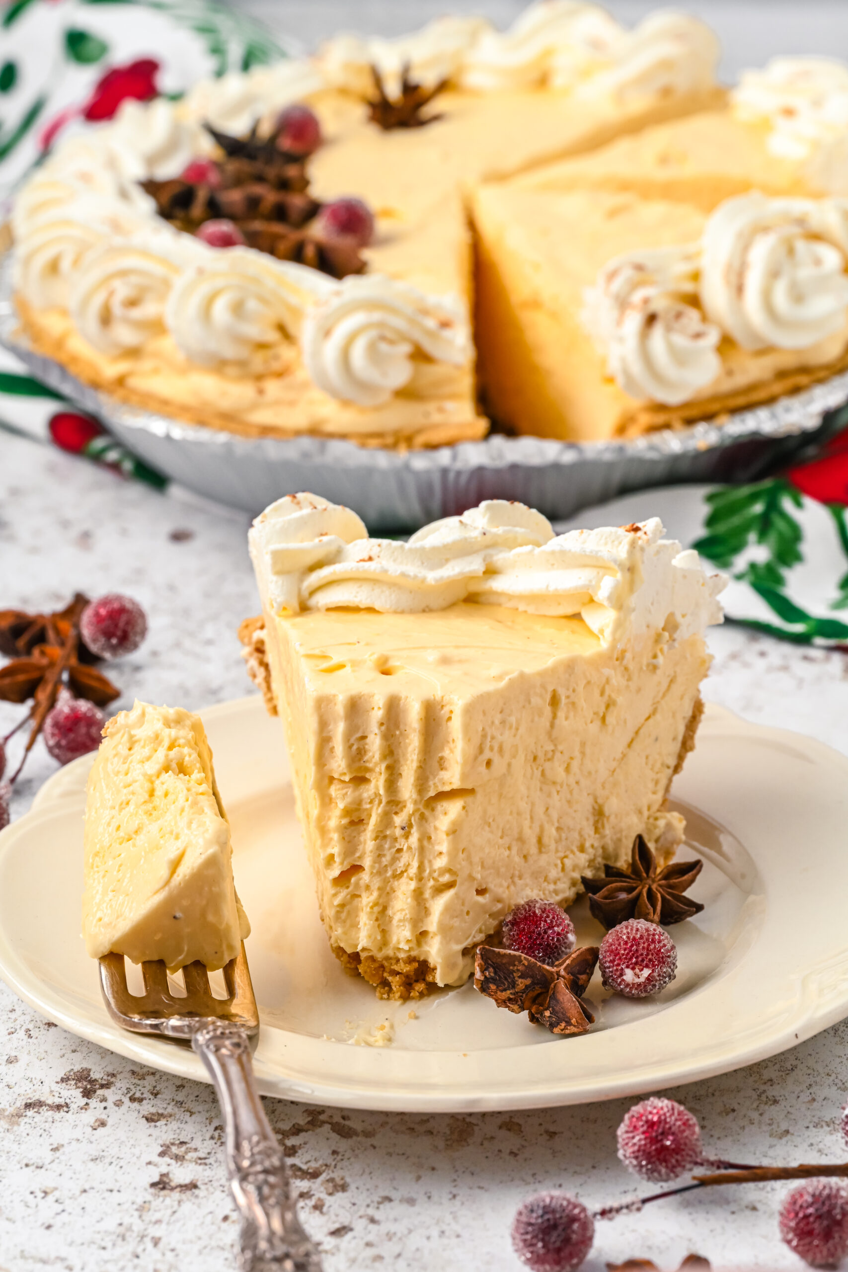 A piece of pie on a white dish with a silver fork removing a piece showing the fluffy inside of the eggnog pie.