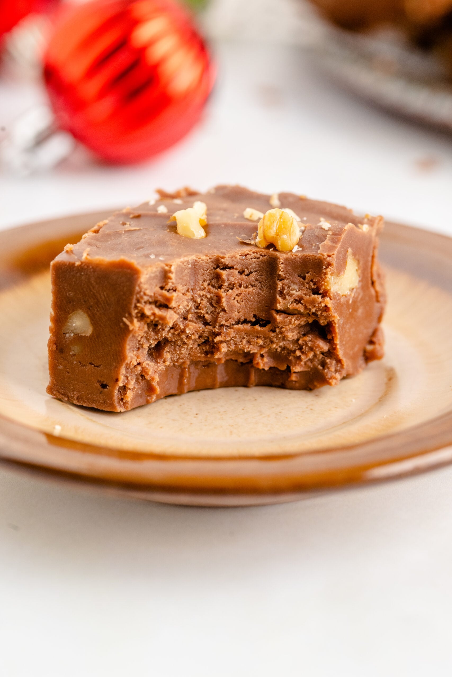 A piece of fantasy fudge on a brown plate with a bite removed showing the inside.