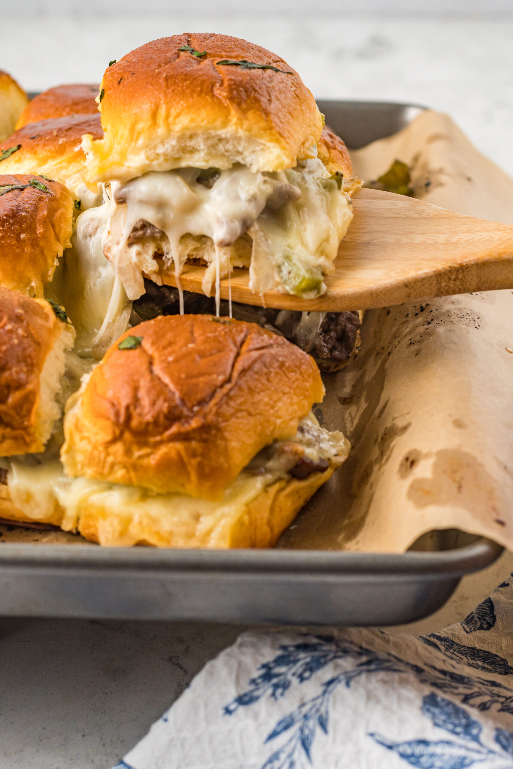 A Philly Cheesesteak Slider being removed from a baking sheet with a wooden spatula. 