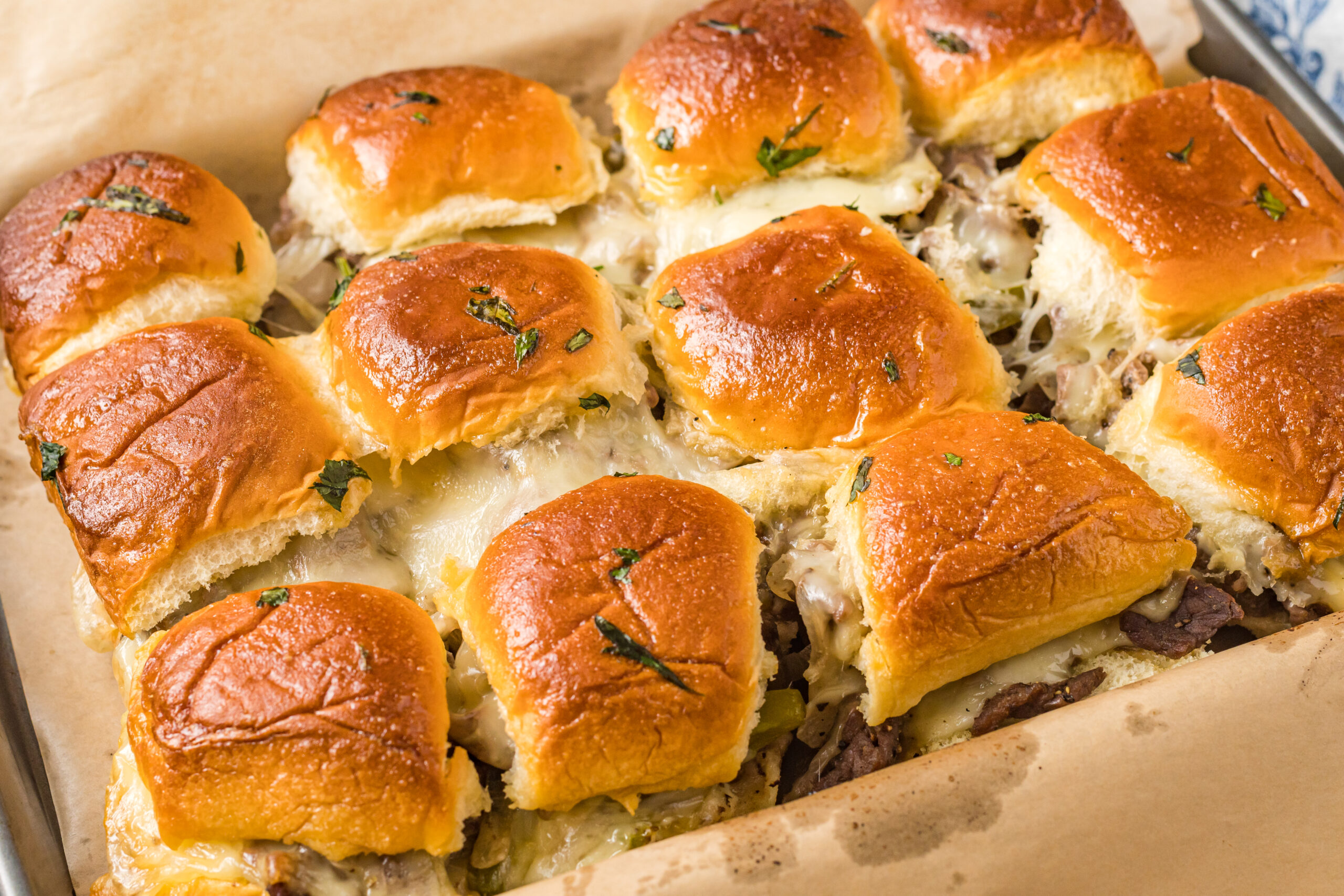 Philly Cheesesteak Sliders on a baking sheet, oozing with melty cheese!